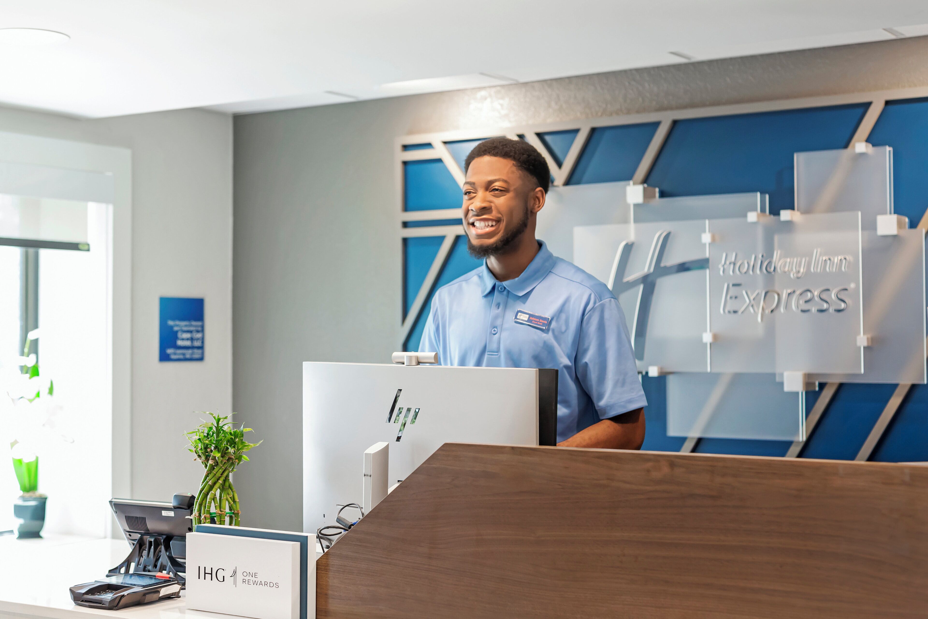 A hotel reception desk with a nameplate for Holiday Inn Express, a computer, and a plant.