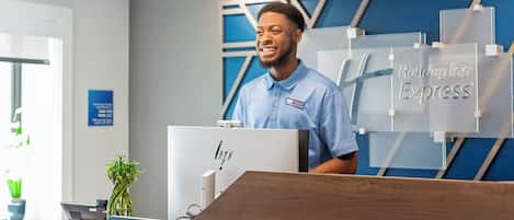 A hotel reception desk with a nameplate for Holiday Inn Express, a computer, and a plant.