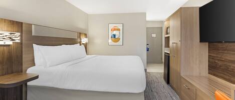 A hotel room with a large bed, a flat-screen TV, a wardrobe, and a desk.
