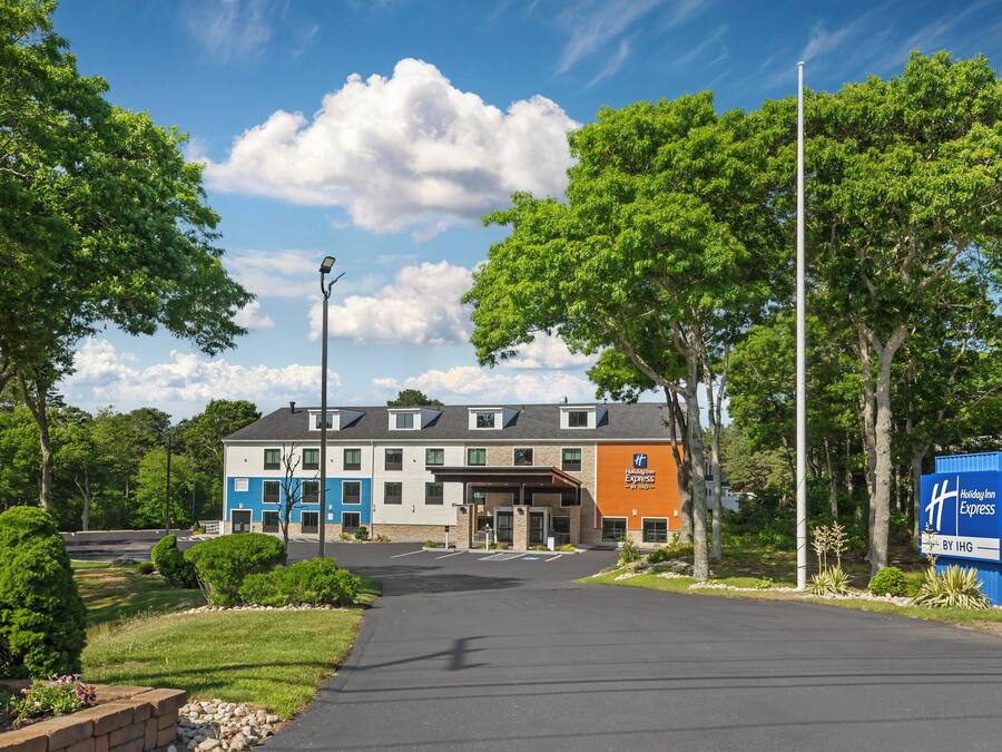 A Holiday Inn Express hotel with a modern design, featuring a central entrance, a parking lot, and a well-maintained surrounding area with trees and landscaping.