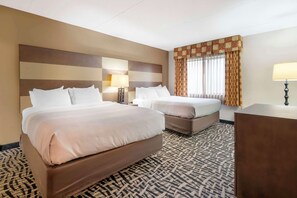 A hotel room with two beds, a patterned carpet, a large headboard, a window with curtains, and a bedside table with a lamp. - Quality Inn & Suites Mayo Clinic Area (Rochester)