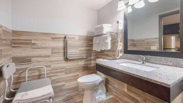 Une salle de bain moderne avec un plancher en bois, des toilettes blanches, un lavabo avec un comptoir en granit, un miroir avec éclairage intégré et un porte-serviettes avec des serviettes pliées.