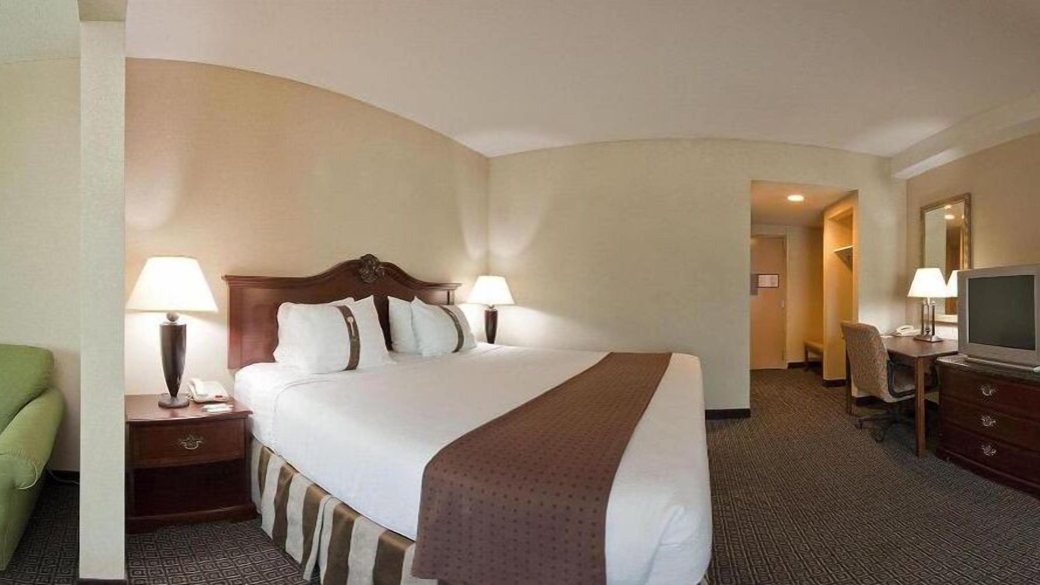 A hotel room with a large bed, two bedside tables with lamps, a television, and a desk with a chair.