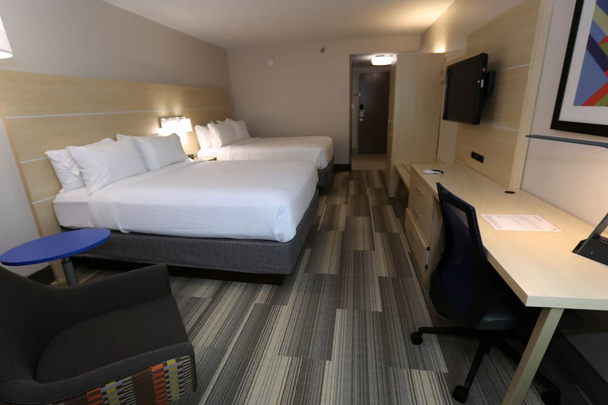A hotel room with two beds, a desk, a chair, a TV, and a small table.