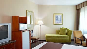 A hotel room with a bed, a desk, a chair, a television, a microwave, a refrigerator, a lamp, and a framed picture on the wall.