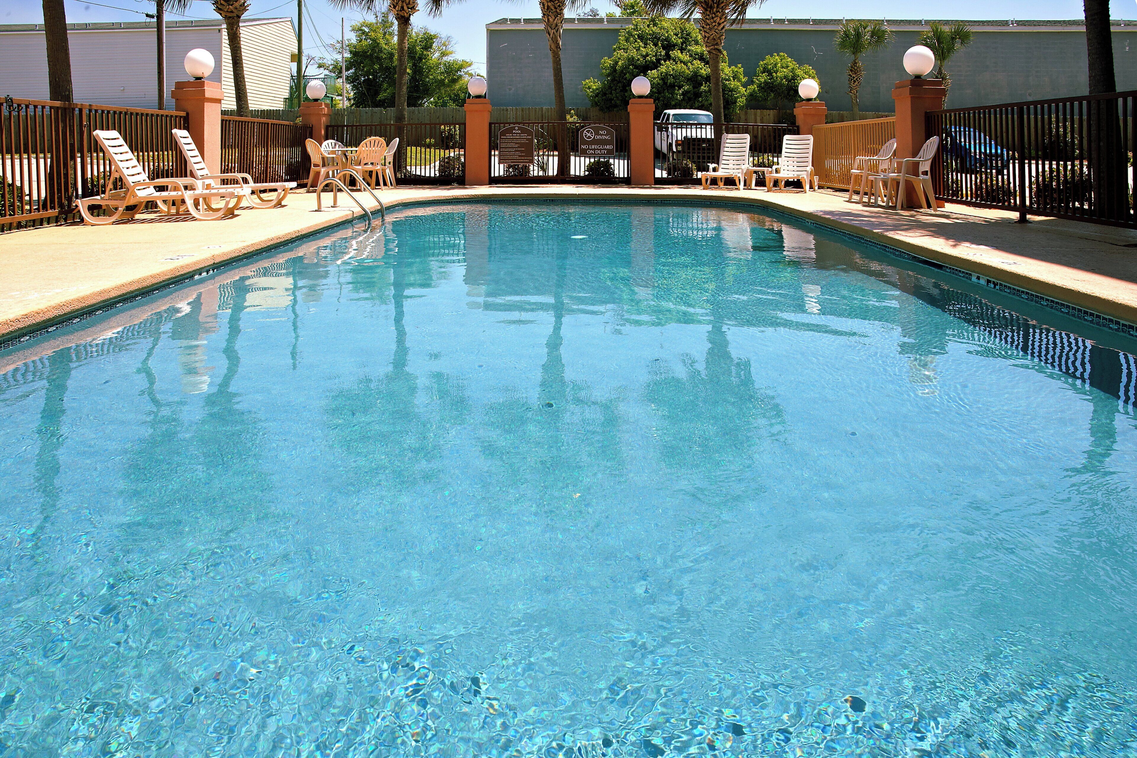 A clear swimming pool with lounge chairs and a fence.