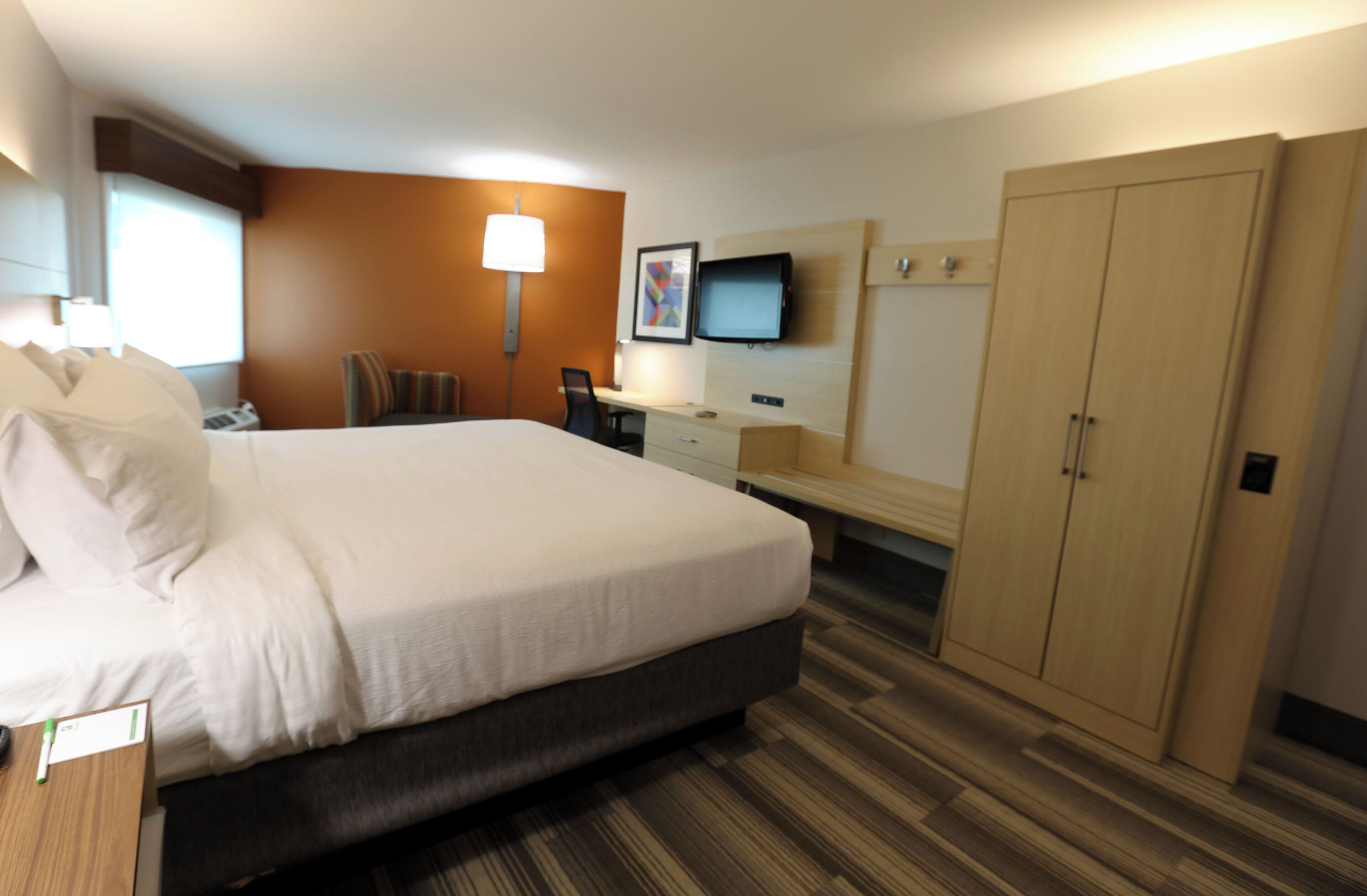 A hotel room with a large bed, a desk, a chair, a television, and a wardrobe.