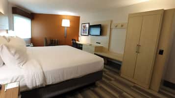 A hotel room with a large bed, a desk, a chair, a television, and a wardrobe.