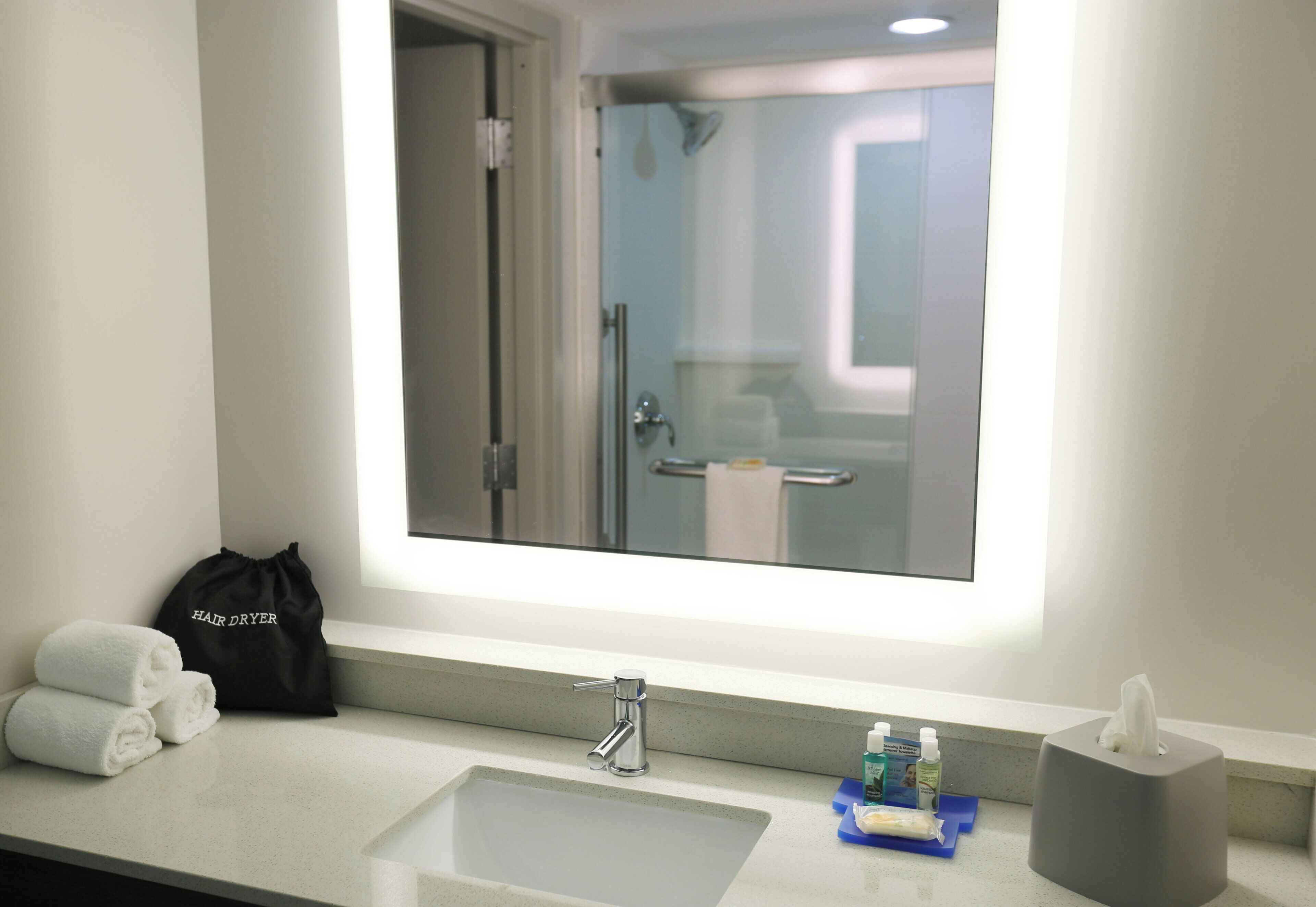 A hotel bathroom with a large mirror, a sink, a towel rack, and toiletries.