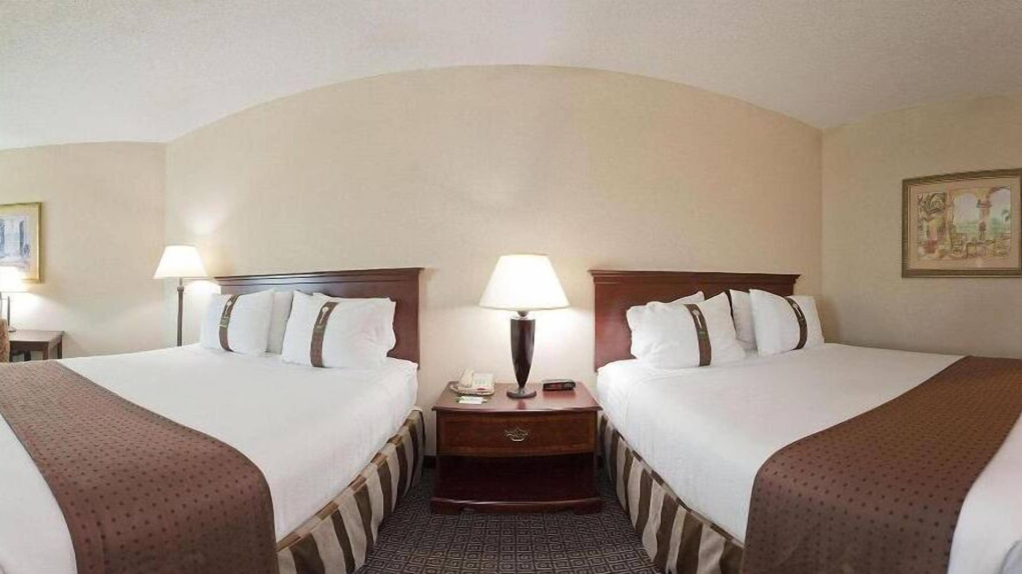 A hotel room with two beds, a nightstand with a lamp, a phone, and a framed picture on the wall.