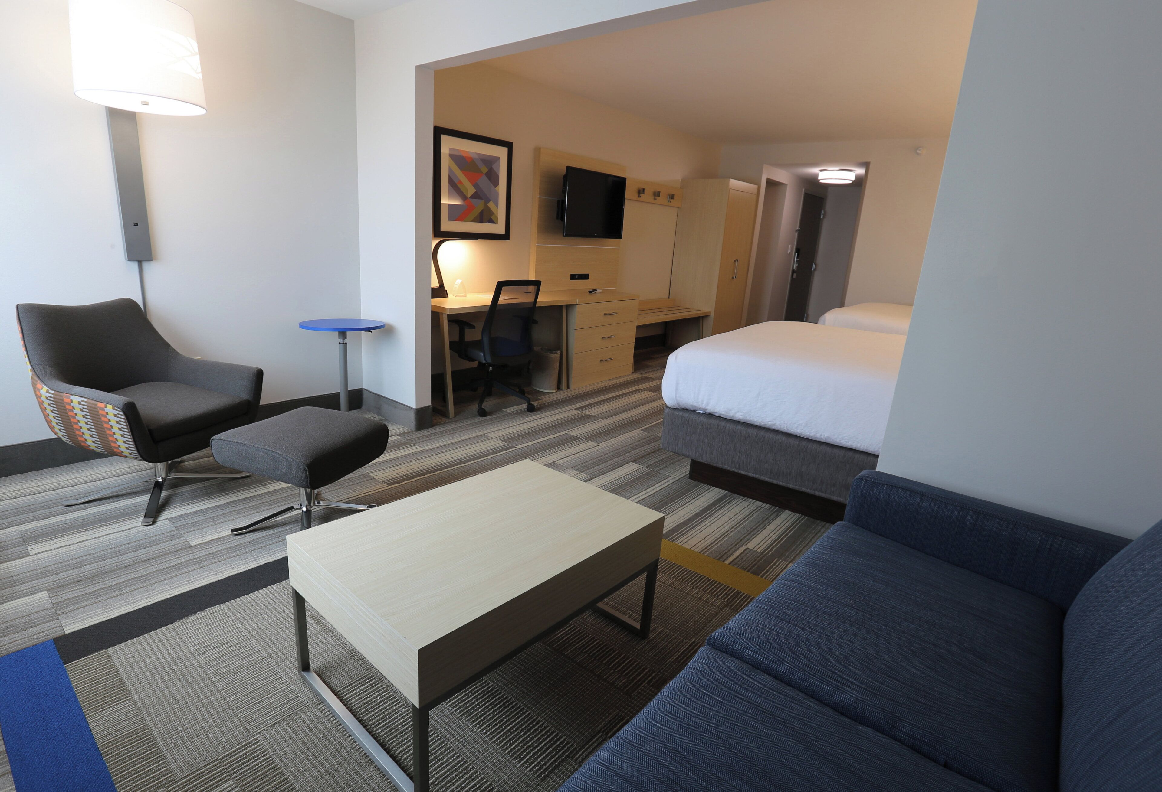 A hotel room with a bed, a desk, a chair, a small table, and a sofa.