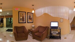 A lobby with two brown armchairs, a computer desk with a monitor, framed pictures on the wall, and an exit sign. - Holiday Inn Express Biloxi - Beach Blvd by IHG (Biloxi)