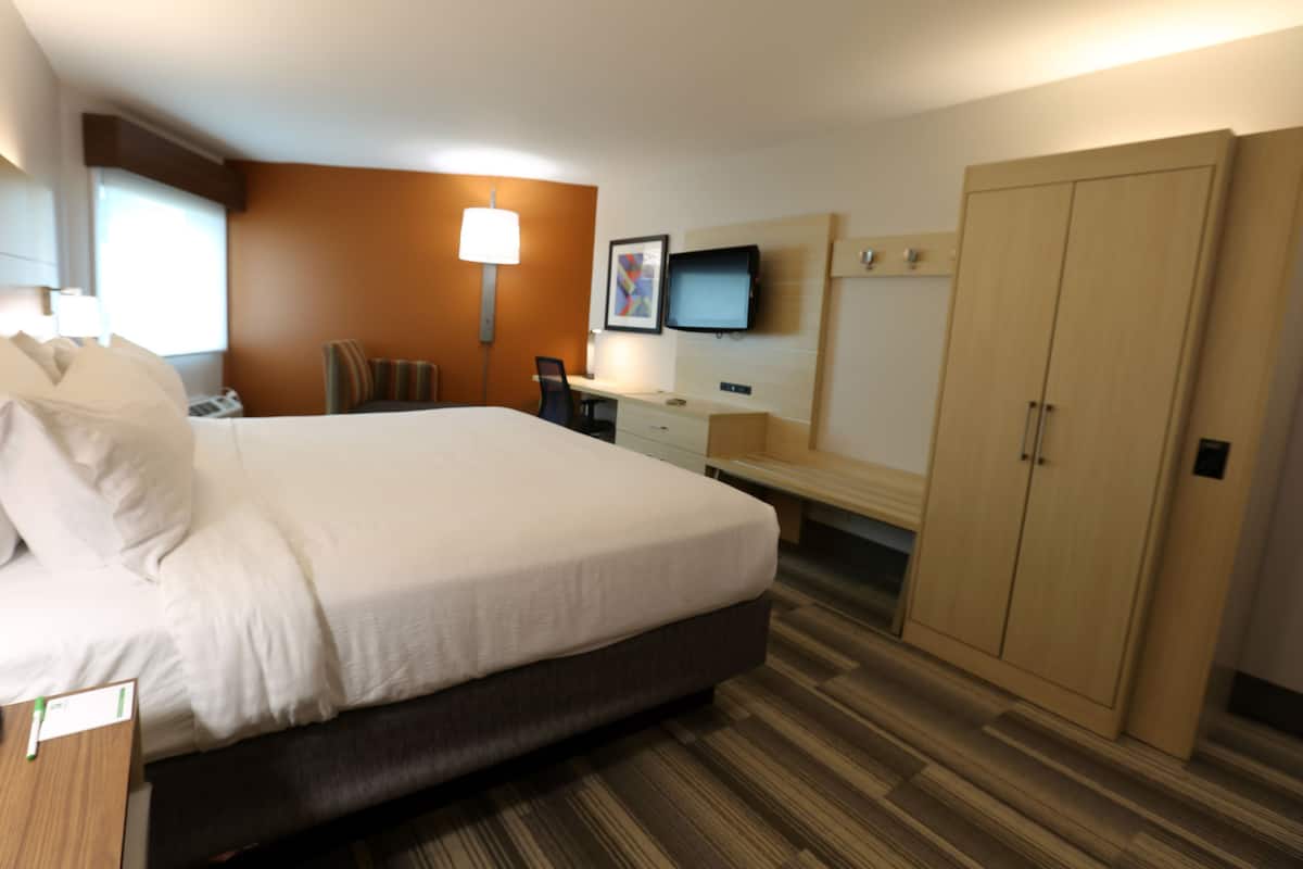 A hotel room with a large bed, a desk with a chair, a television, and a wardrobe.