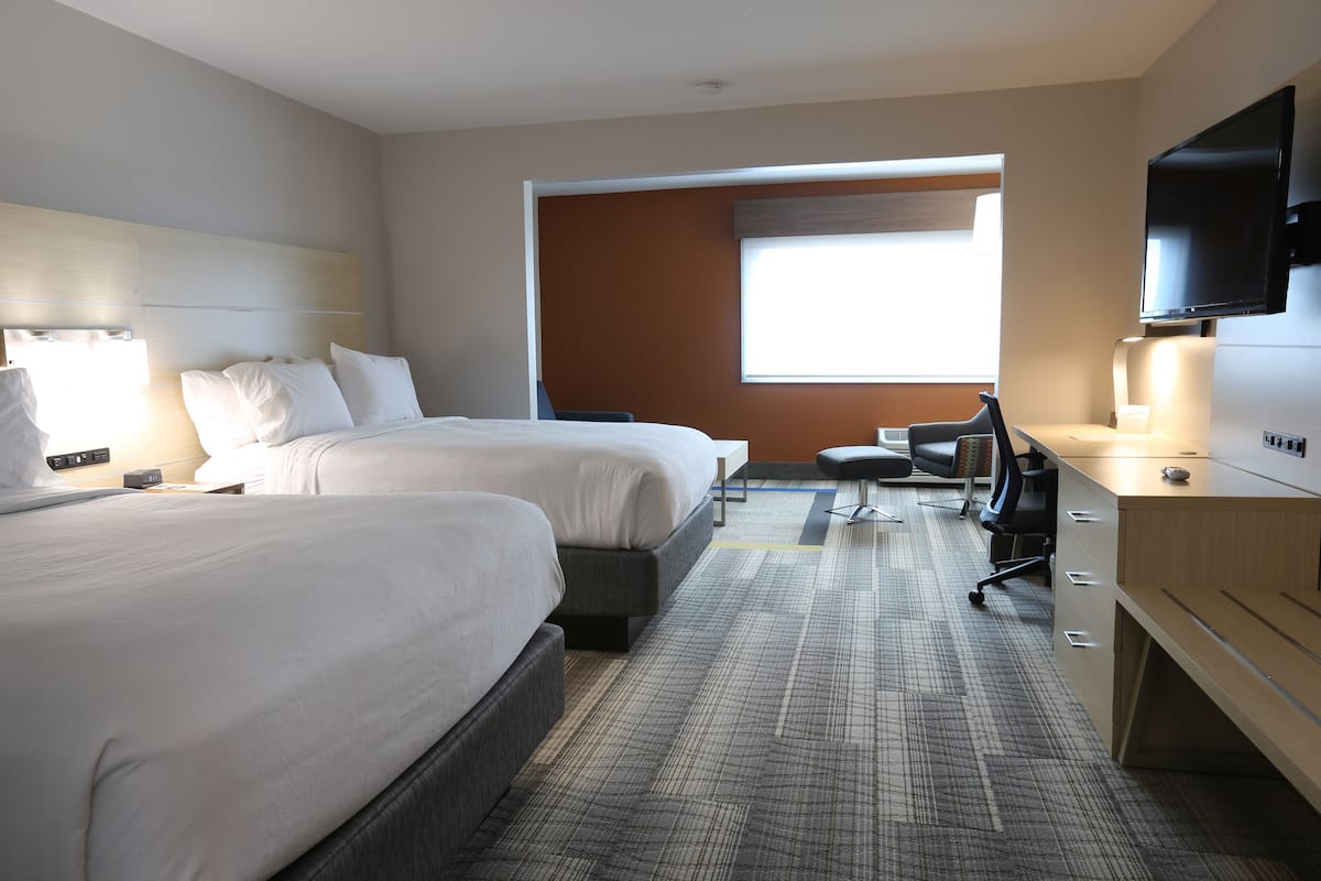A hotel room with two beds, a desk, a chair, a TV, and a window with a view.