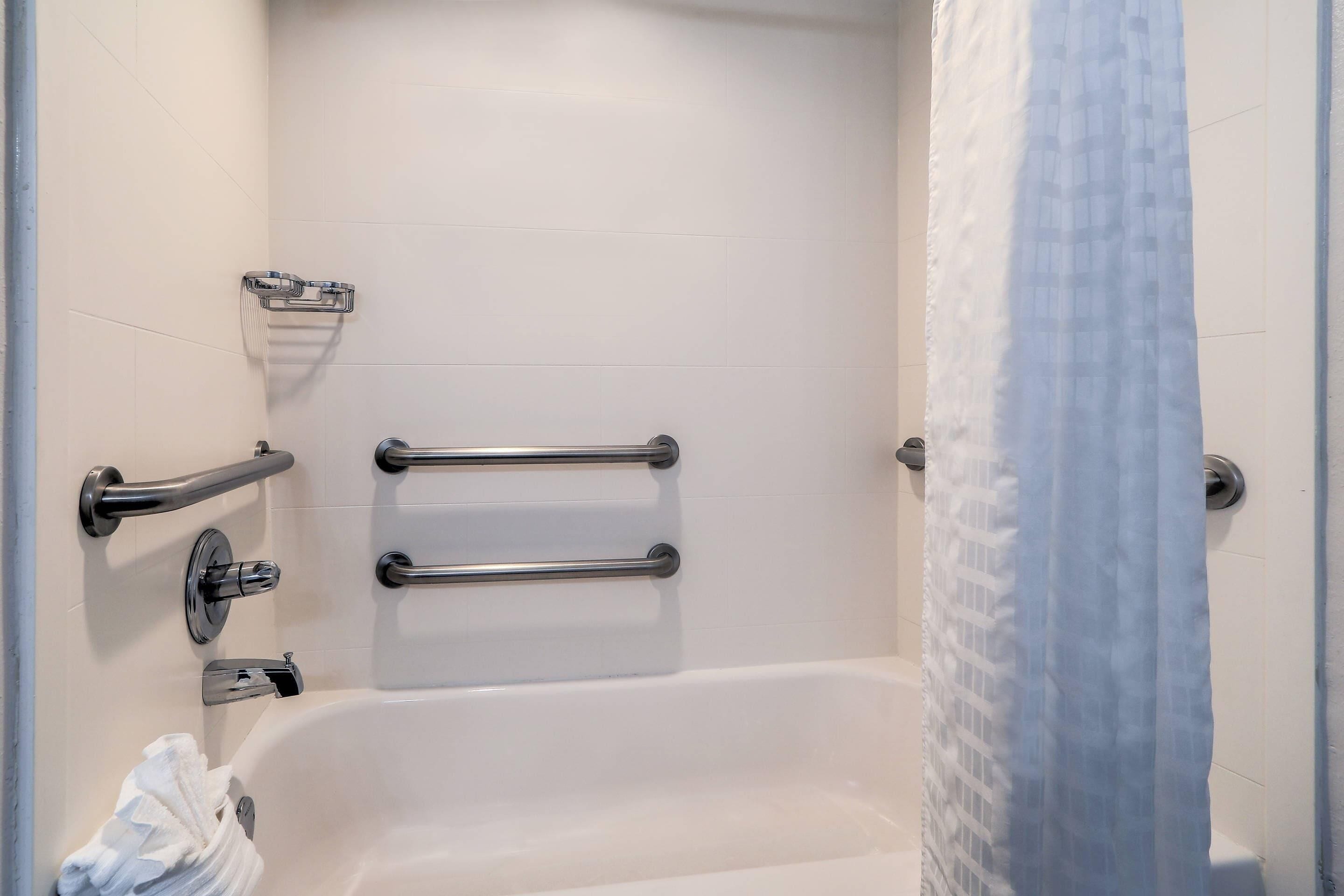 Un baño con bañera, barras de apoyo, un perchero y una cortina de ducha.