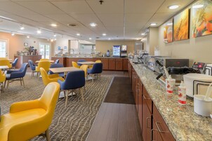 A hotel dining area with yellow and blue chairs, a buffet counter, and a coffee station.