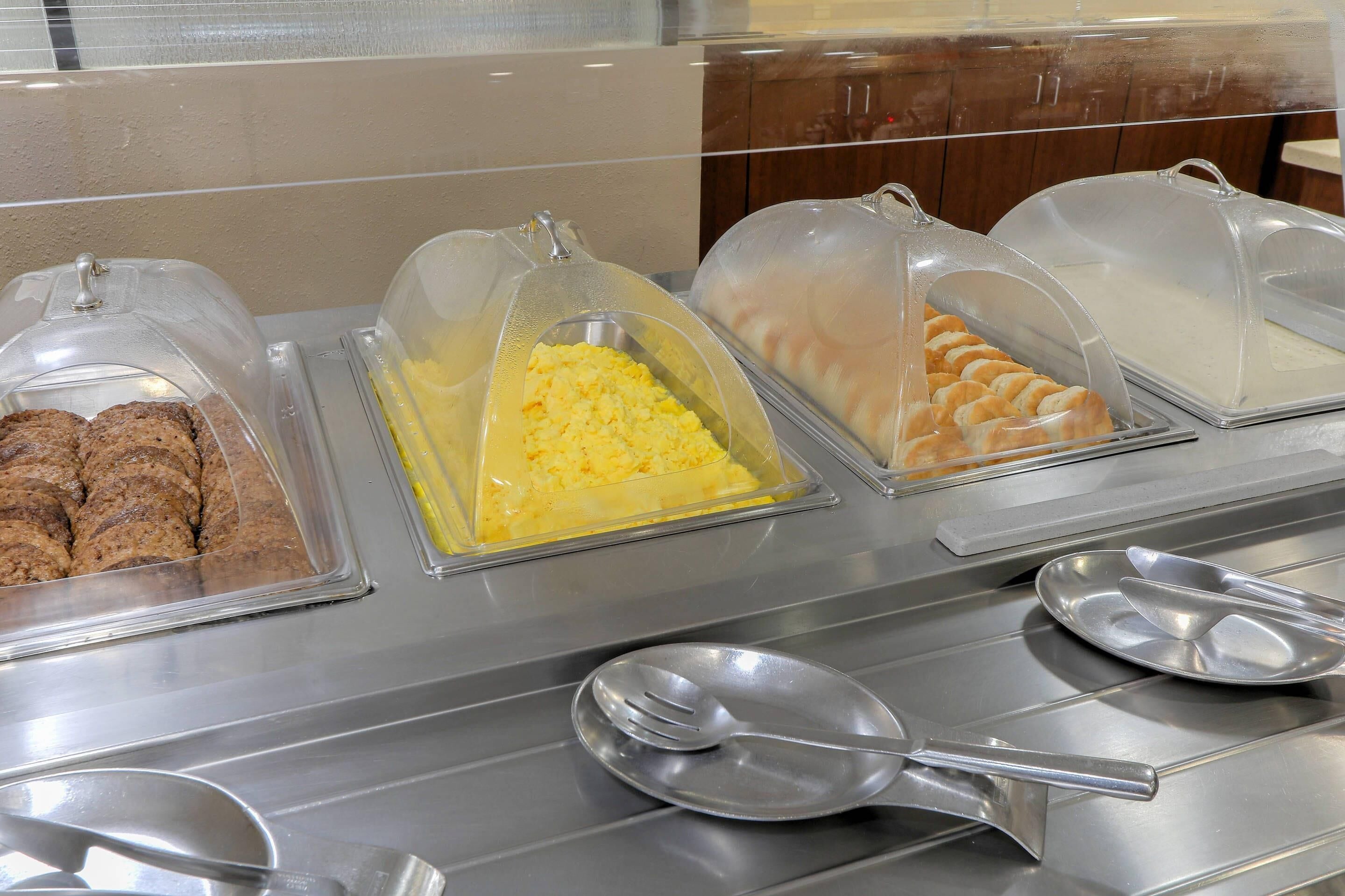 Un buffet avec des plats couverts, comprenant ce qui semble être des œufs brouillés, des viennoiseries et, peut-être, un plat de viande.