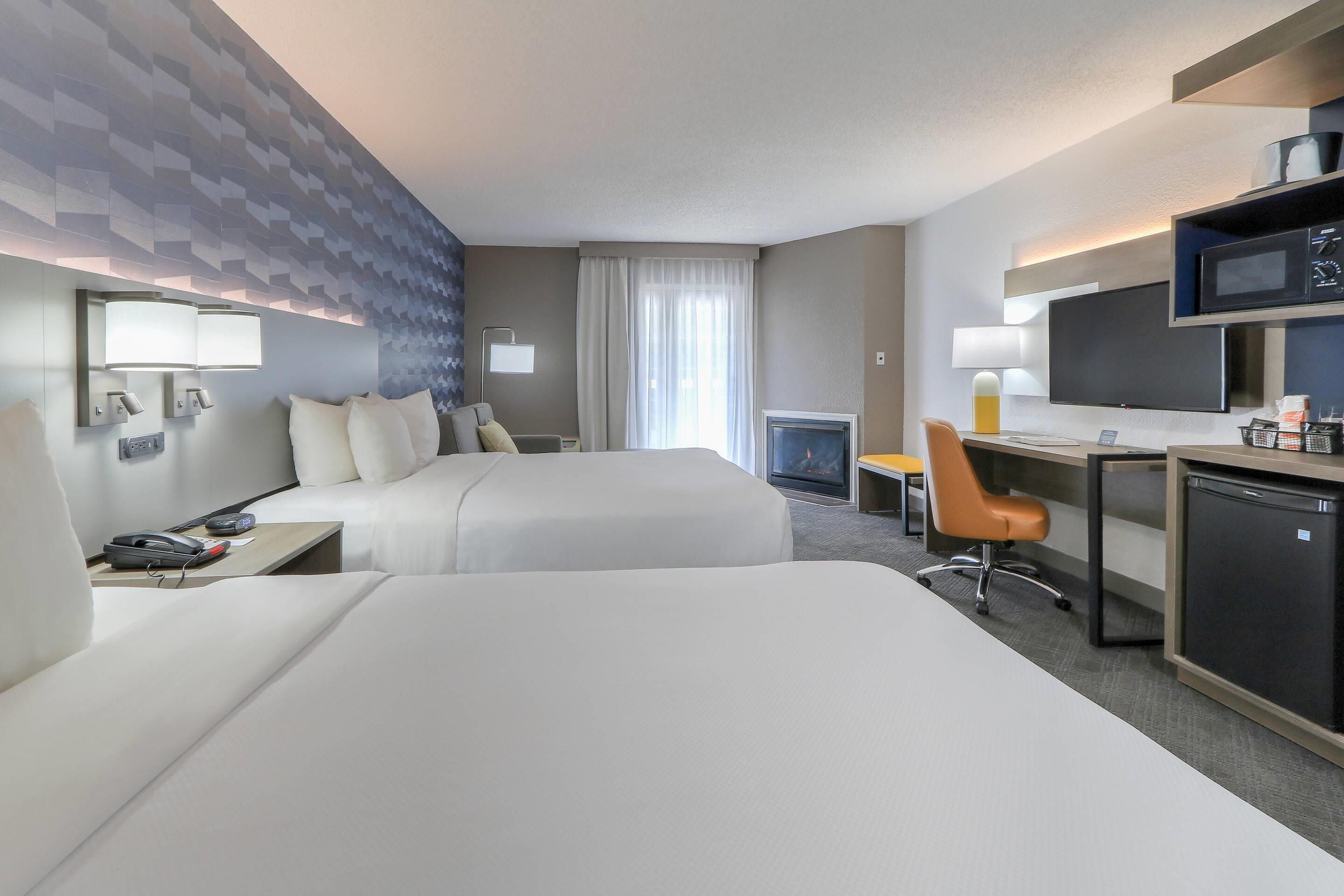 Une chambre d’hôtel avec deux lits, un bureau avec un ordinateur, un four à micro-ondes et une télévision.