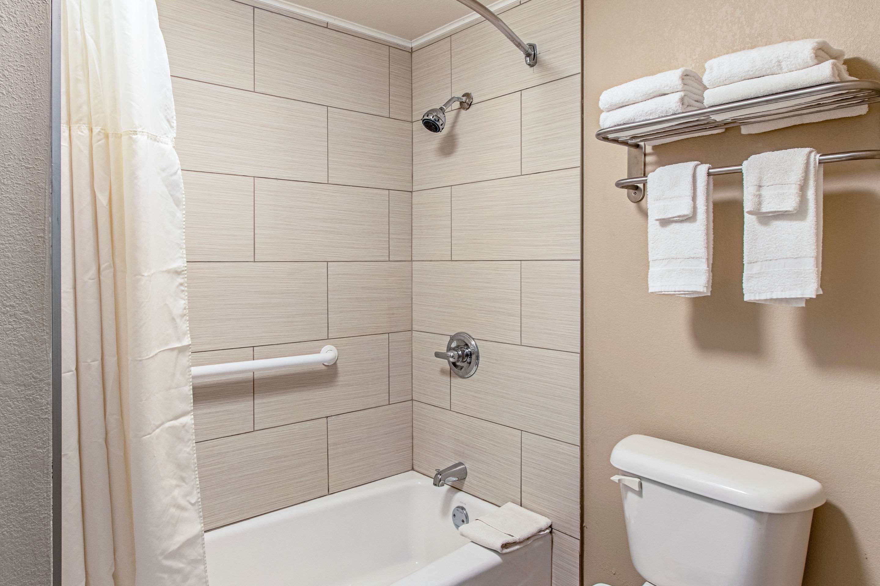 Un baño con bañera, ducha e inodoro. Hay toallas en un perchero y una cortina de ducha.