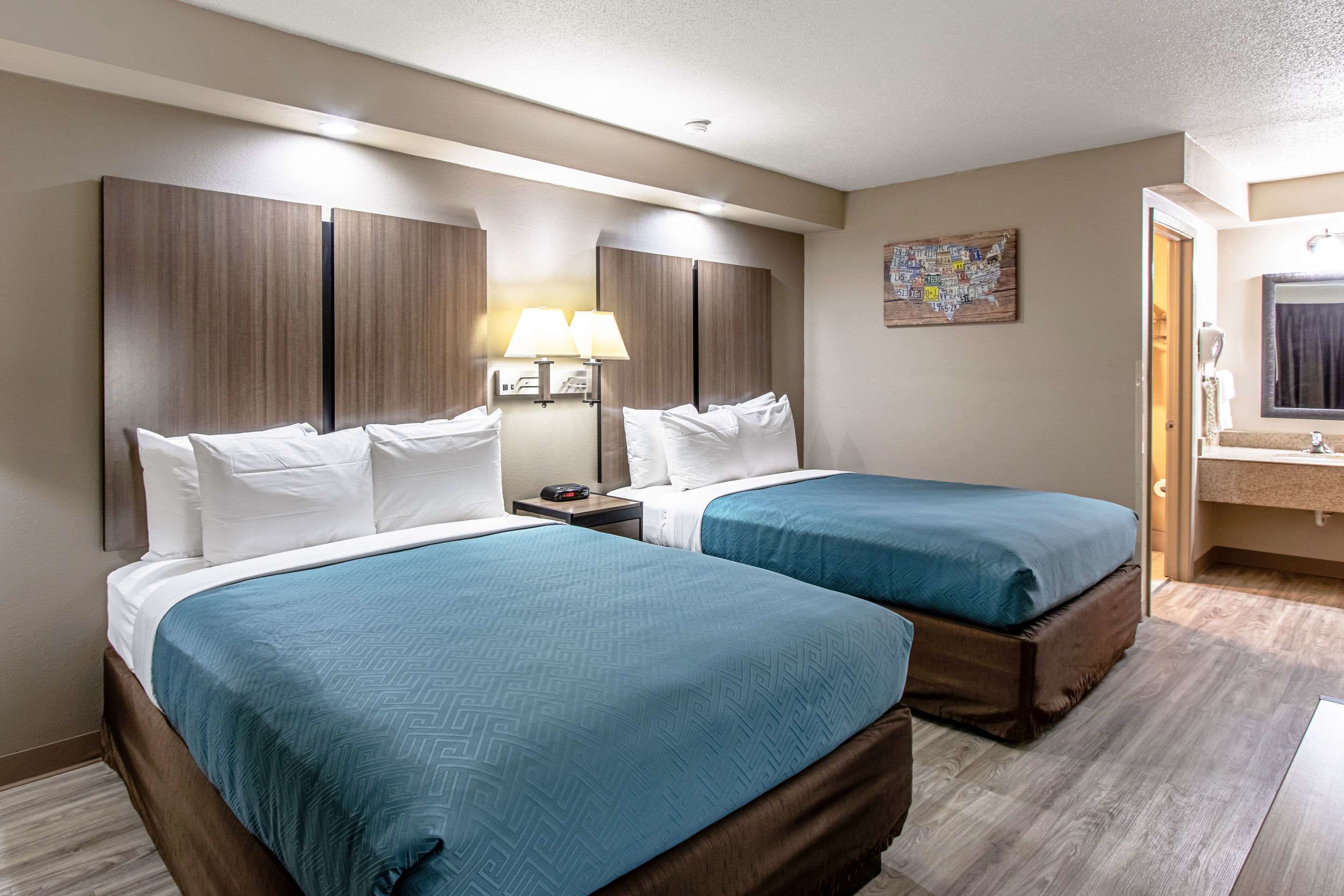Une chambre d’hôtel avec deux lits, une table de chevet avec des lampes, une carte accrochée au mur et une salle de bain visible à travers une porte ouverte.