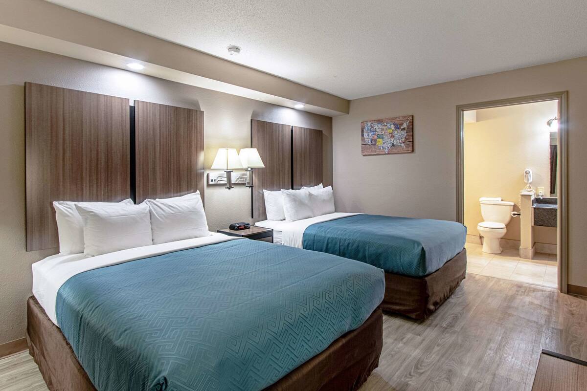 Une chambre d’hôtel avec deux lits, une table de chevet, une lampe et une salle de bain visible à travers une porte ouverte.