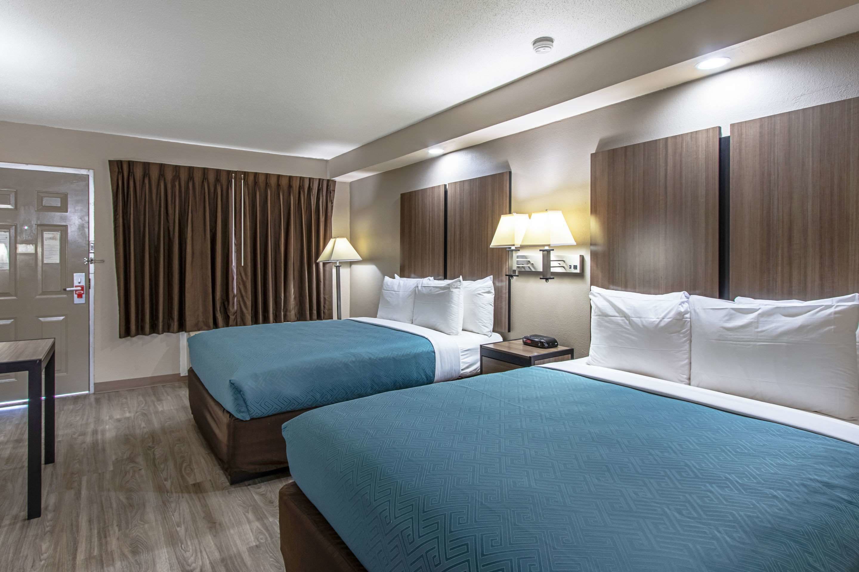 Quarto de hotel com duas camas, uma escrivaninha e uma porta.