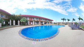 A swimming pool with a curved edge, surrounded by a concrete deck. There are lounge chairs and a building with a red roof in the background. - Econo Lodge Kingsville (Kingsville)
