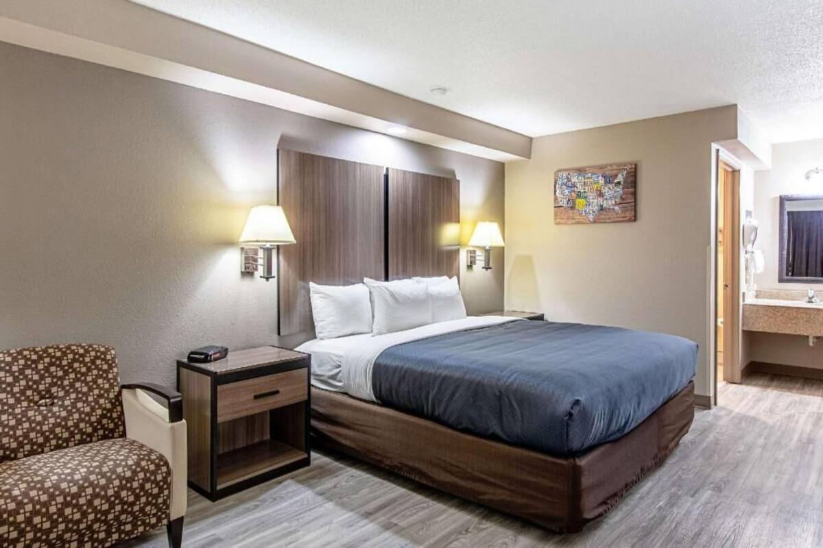 Une chambre d’hôtel comprenant un lit, des tables de chevet, une chaise, un bureau, une œuvre d’art représentant une carte et une salle de bain avec un miroir et un lavabo.