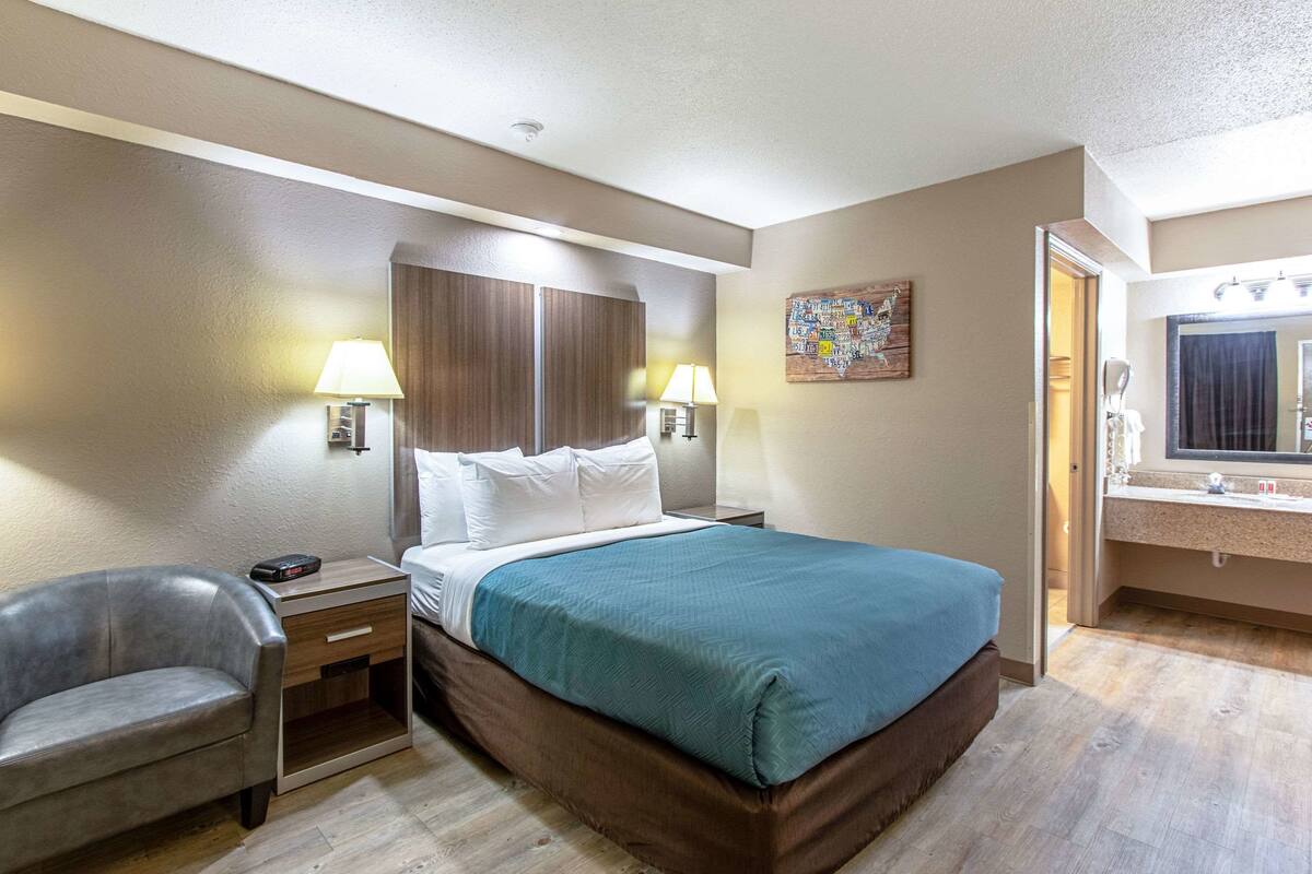 Une chambre d’hôtel comprenant un lit, des tables de chevet, une chaise et une salle de bain avec un miroir et un lavabo.