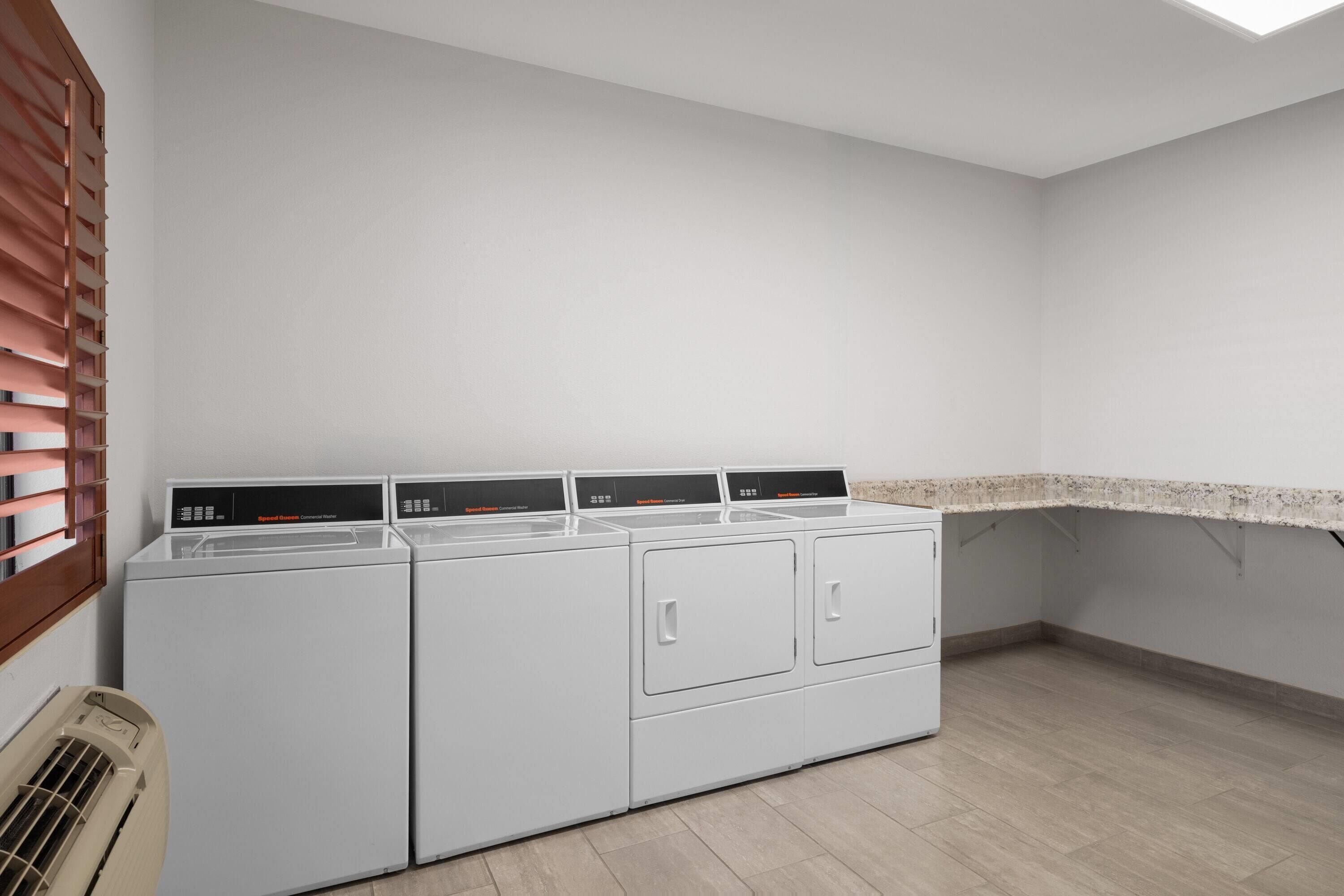 A laundry room with four stacked washers and dryers, a vent, and a countertop.