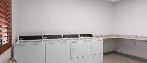 A laundry room with four stacked washers and dryers, a vent, and a countertop.