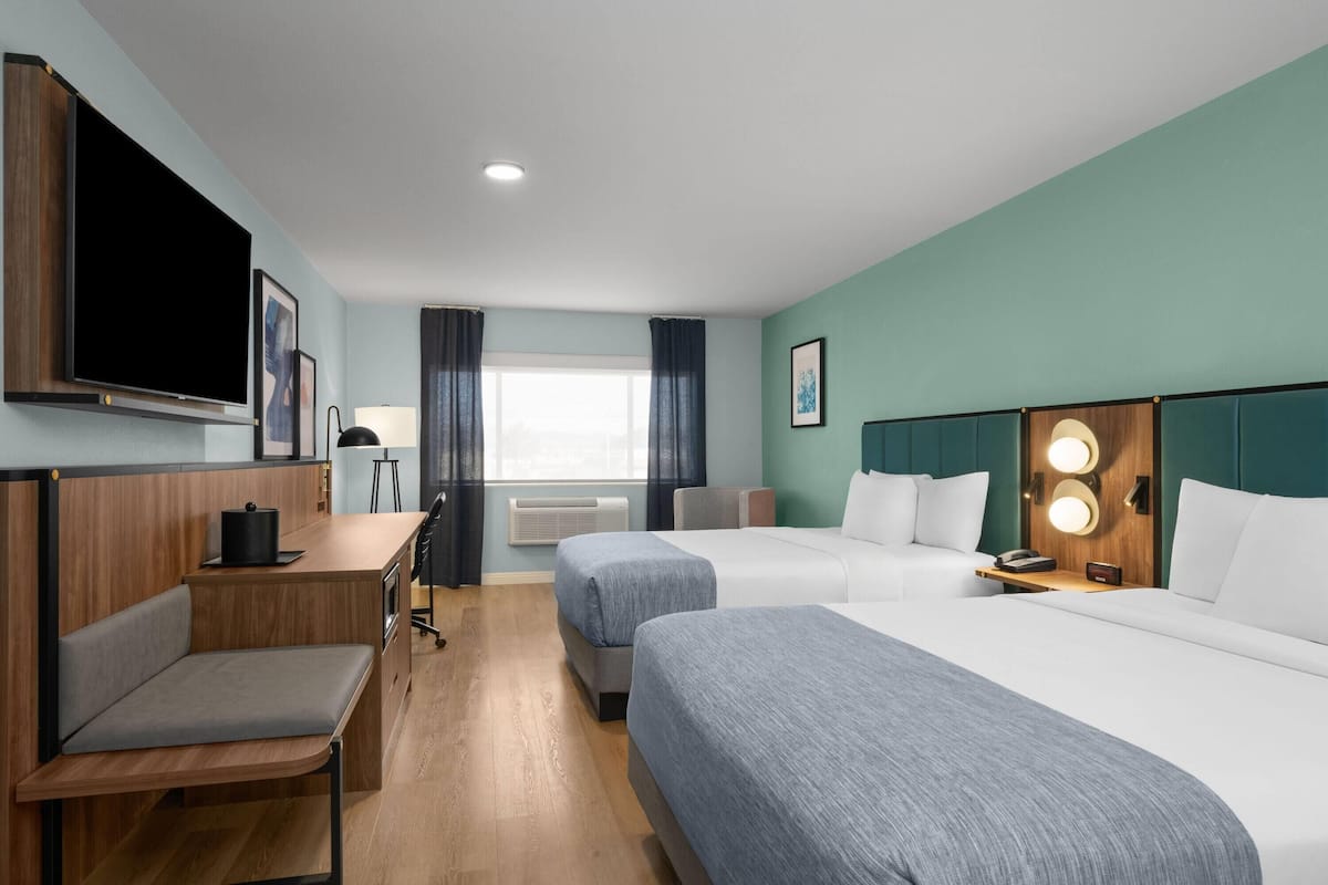 Quarto de hotel com uma cama, uma escrivaninha, uma cadeira, uma televisão e uma janela com cortinas.