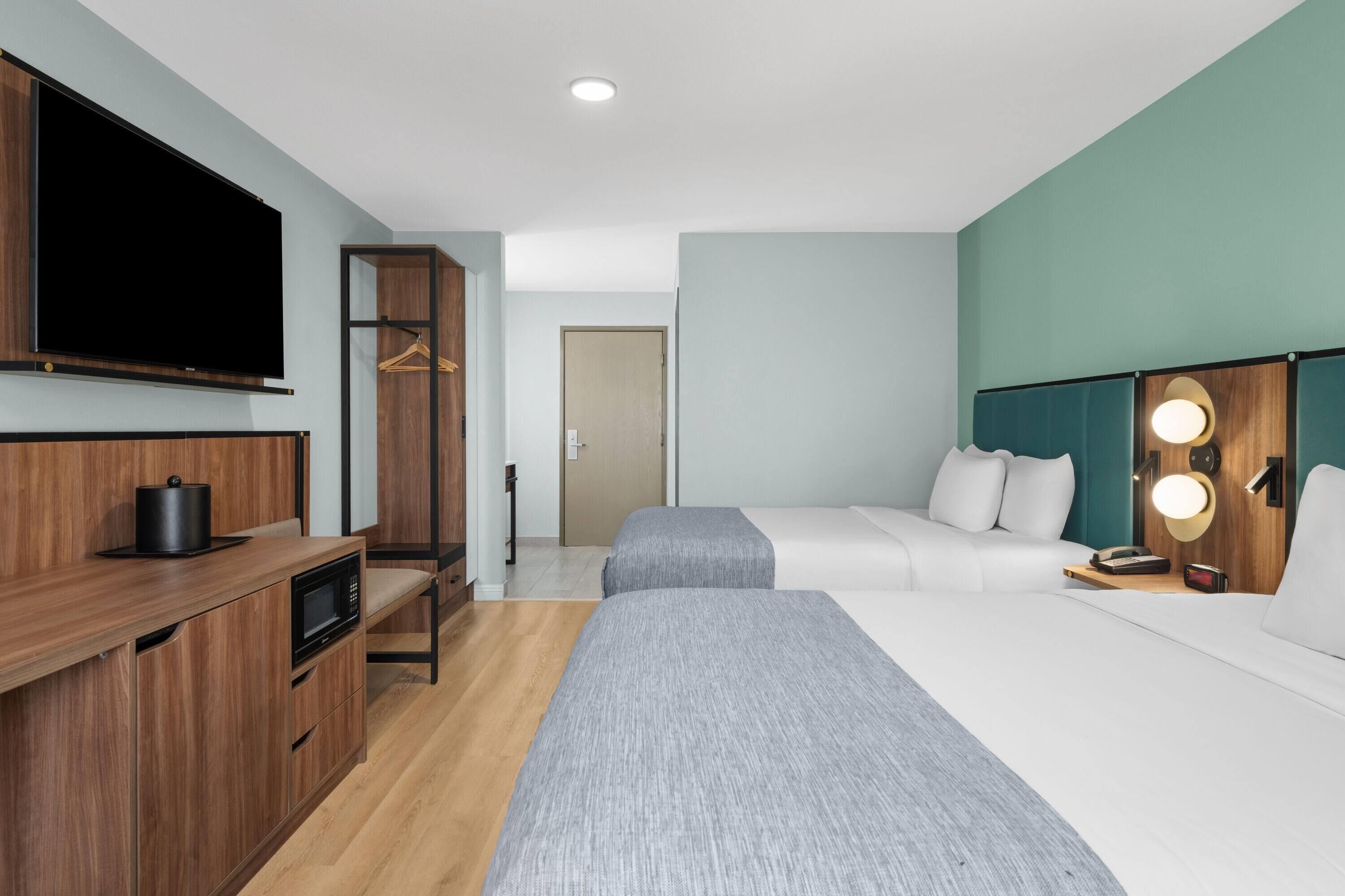 Ett hotellrum med TV, ett litet kök, två sängar och en garderob.