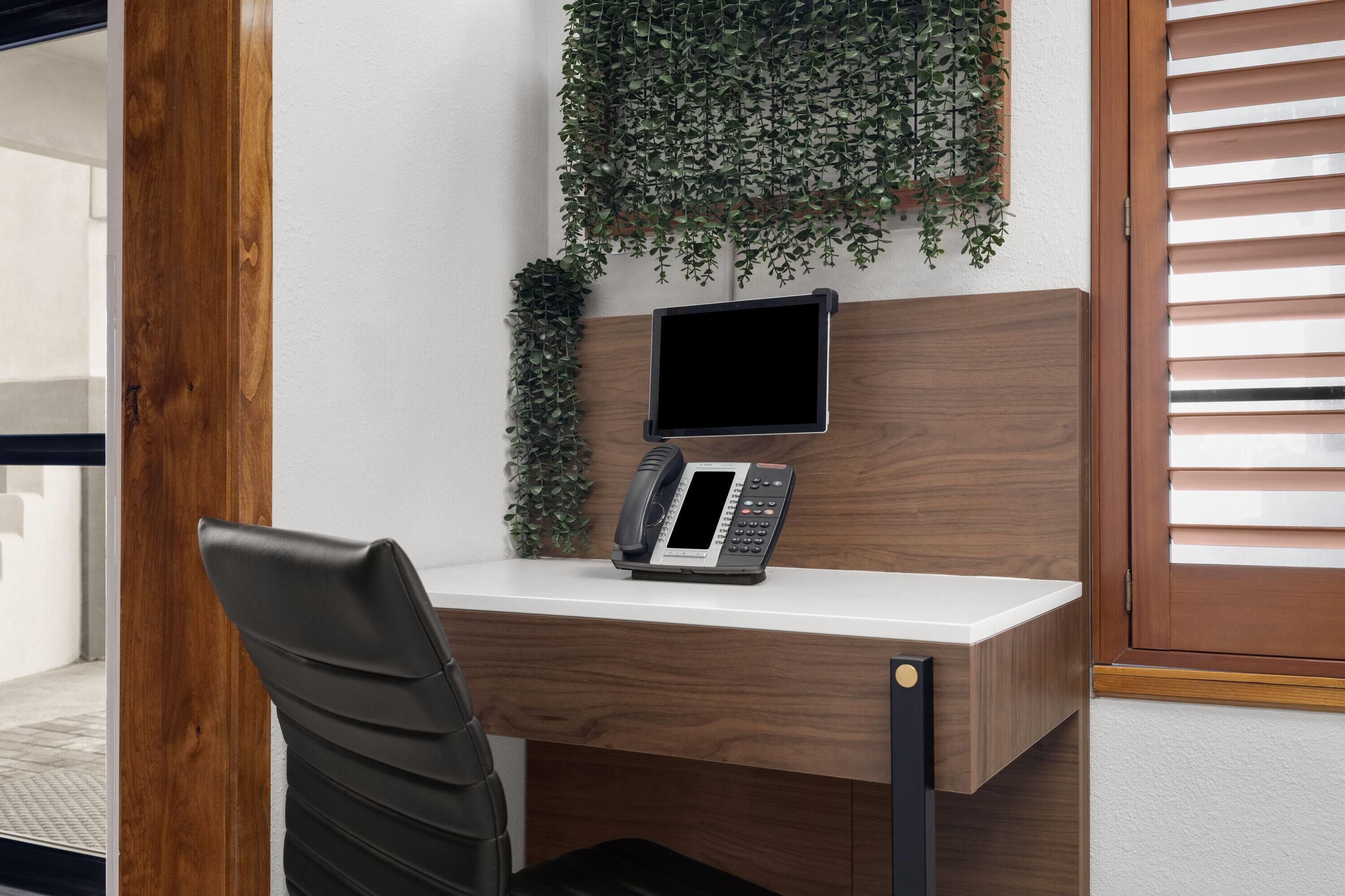 A modern office desk with a telephone, a monitor, and a plant.