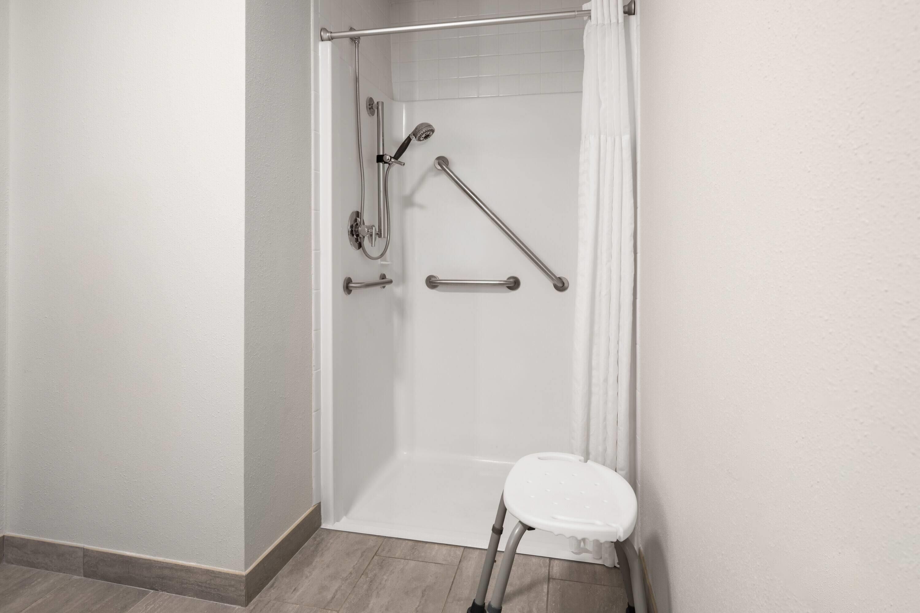 A shower area with a white bathtub, grab bars, and a white step stool.