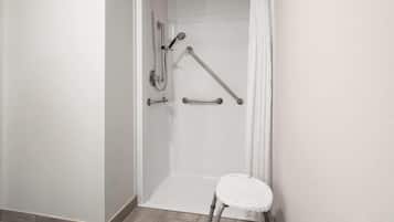 A shower area with a white bathtub, grab bars, and a white step stool.