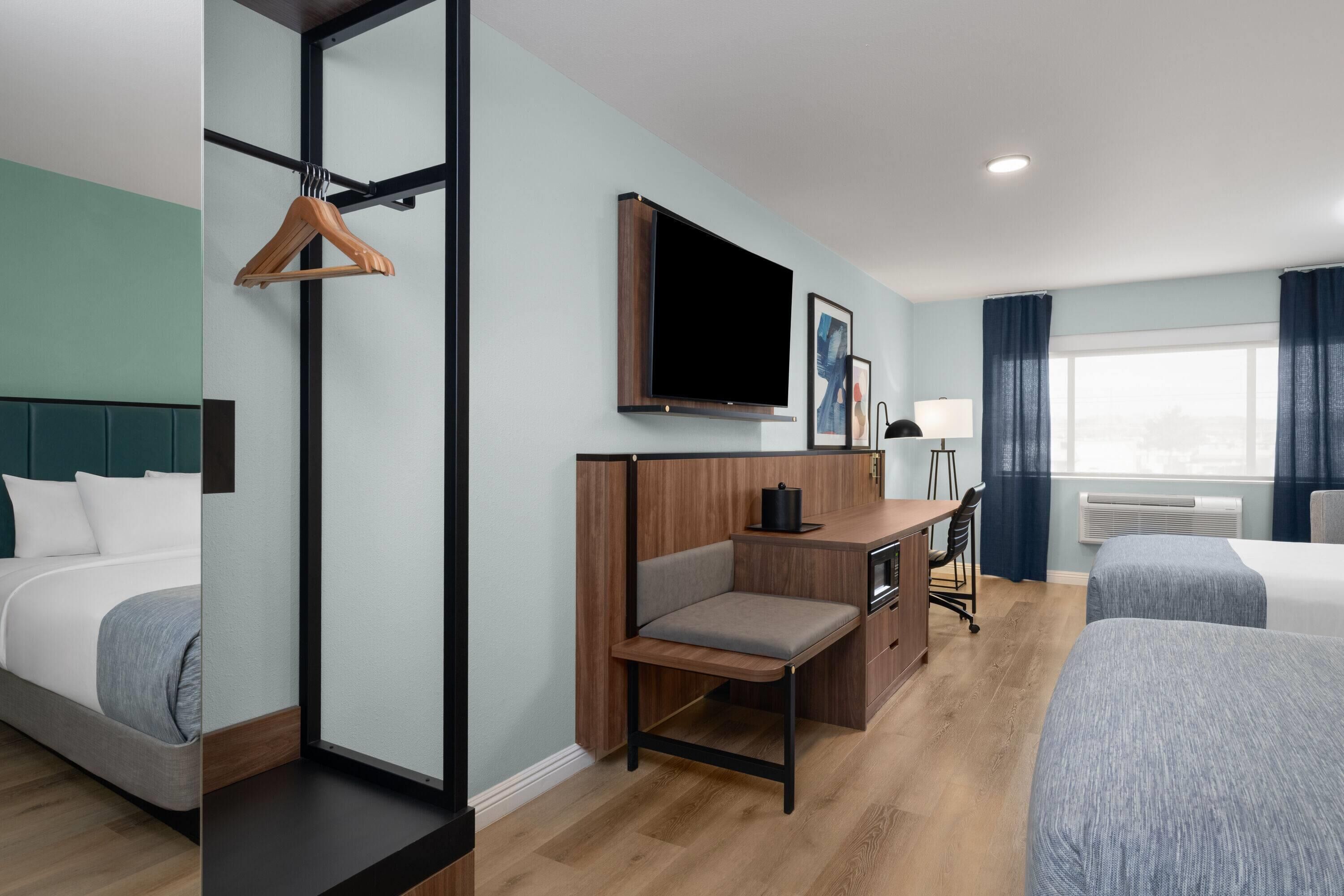 A hotel room with a bed, a desk, a chair, a TV, and a window with curtains.