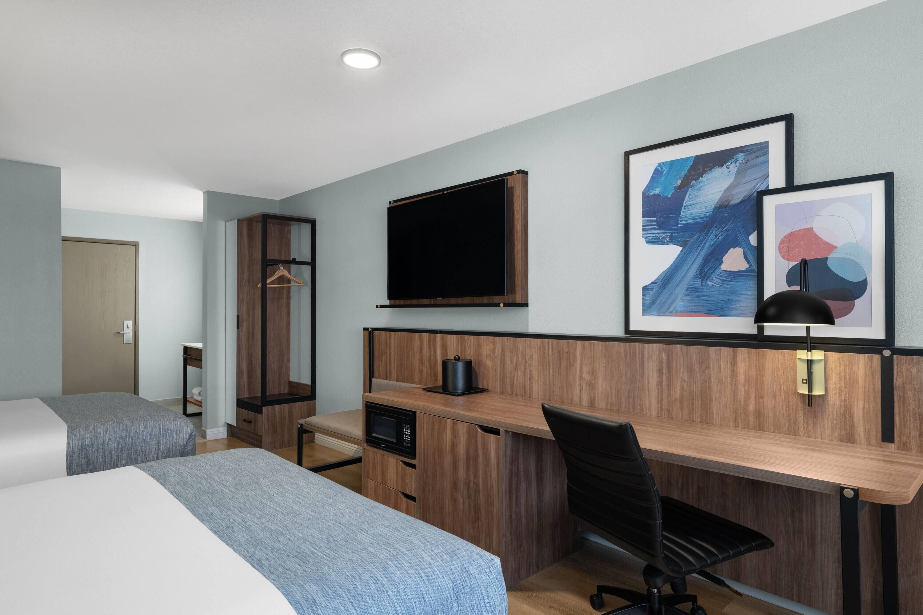 Een hotelkamer met twee bedden, een bureau, een stoel, een televisietoestel en kunst aan de muur.