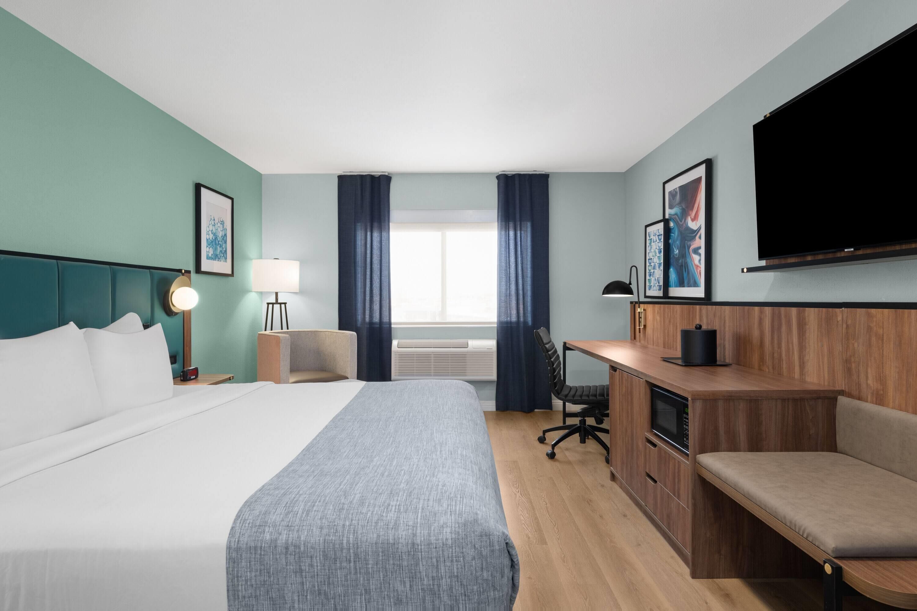 Habitación de hotel con cama, escritorio, silla, televisión y obras de arte.