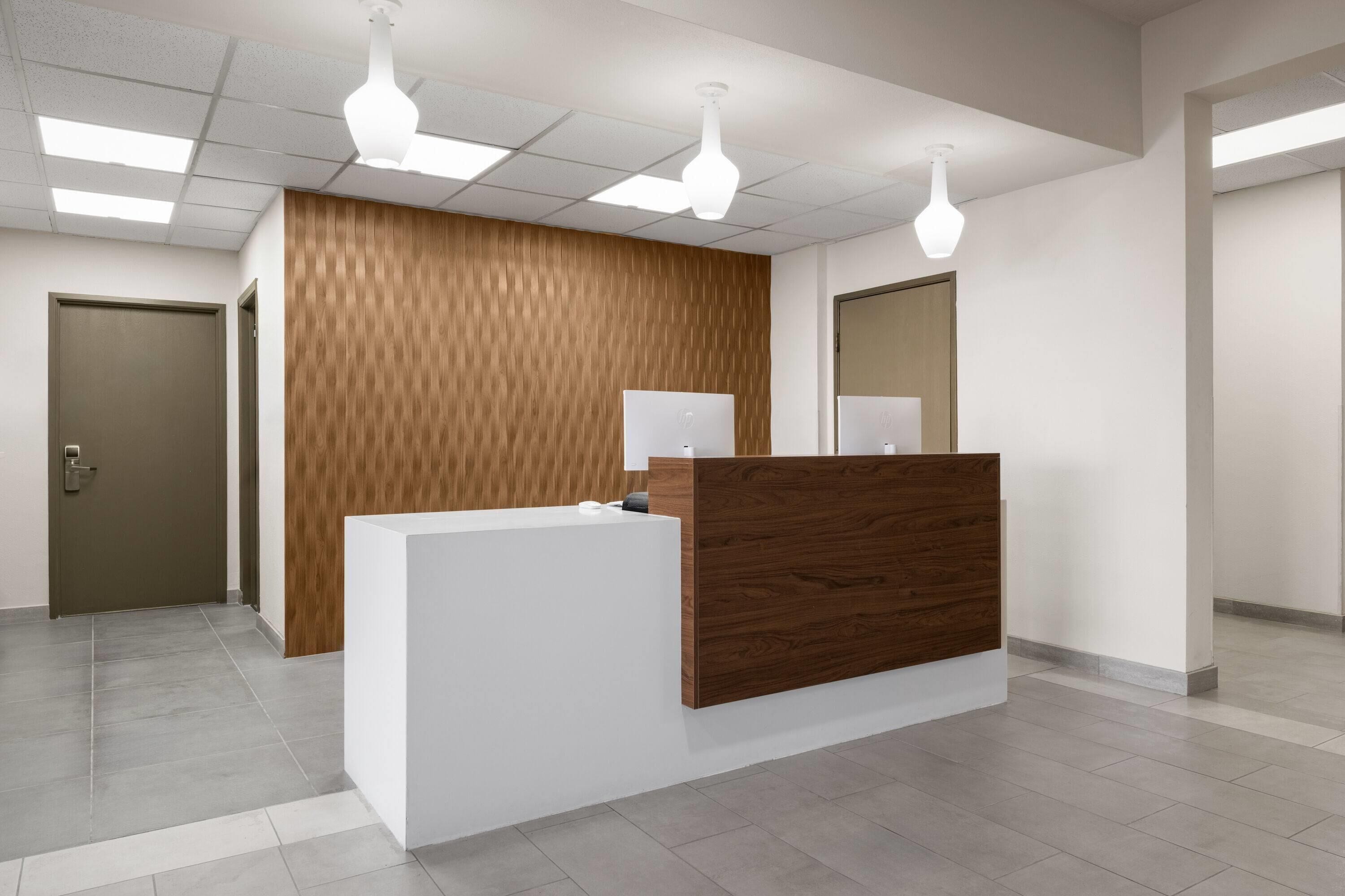 Un área de recepción con un mostrador de madera, una pared blanca e iluminación empotrada en el techo.