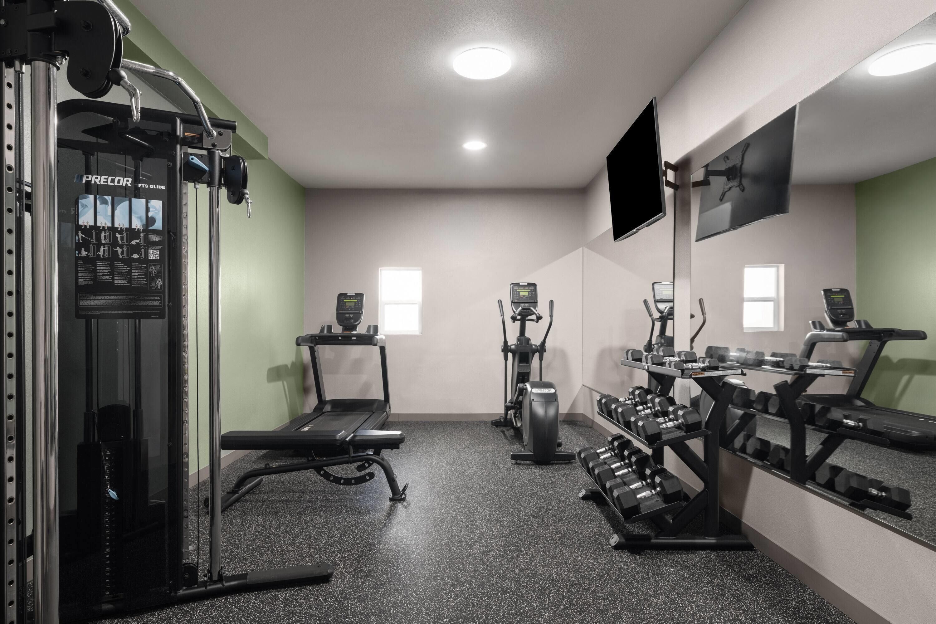 Un gimnasio con cinta de correr, elíptica, banco de pesas y mancuernas.