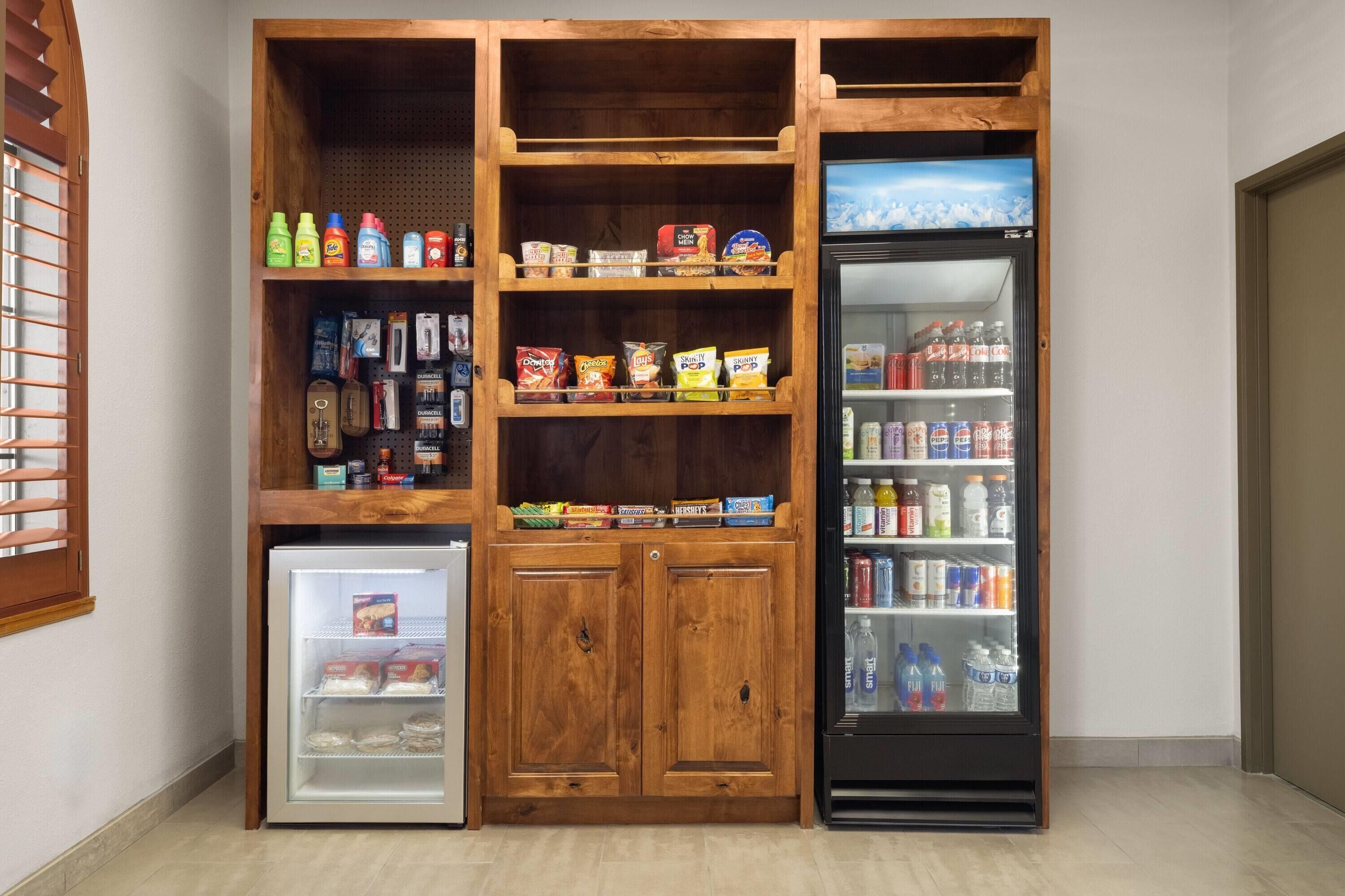 Una kitchenette compacta con un mini refrigerador, un congelador y una unidad de estantes con diversos alimentos y bebidas.