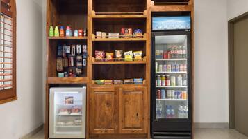 Una kitchenette compacta con un mini refrigerador, un congelador y una unidad de estantes con diversos alimentos y bebidas.