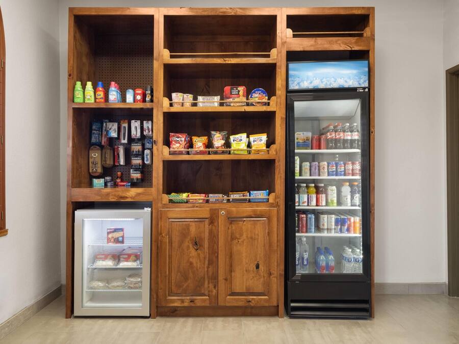 Una kitchenette compacta con un mini refrigerador, un congelador y una unidad de estantes con diversos alimentos y bebidas.