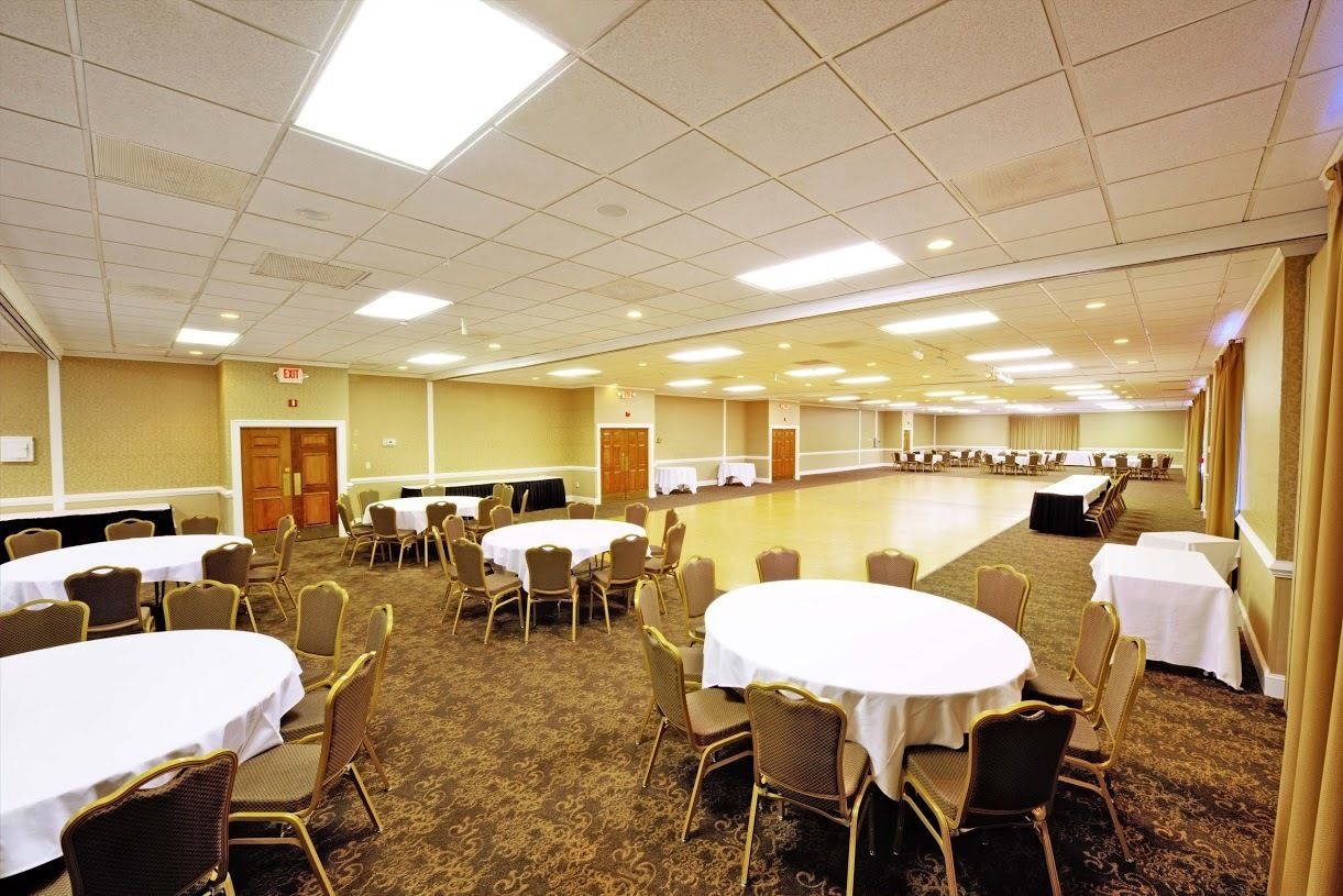 A conference room with round tables and chairs, carpeted floors, and a high ceiling with fluorescent lighting.