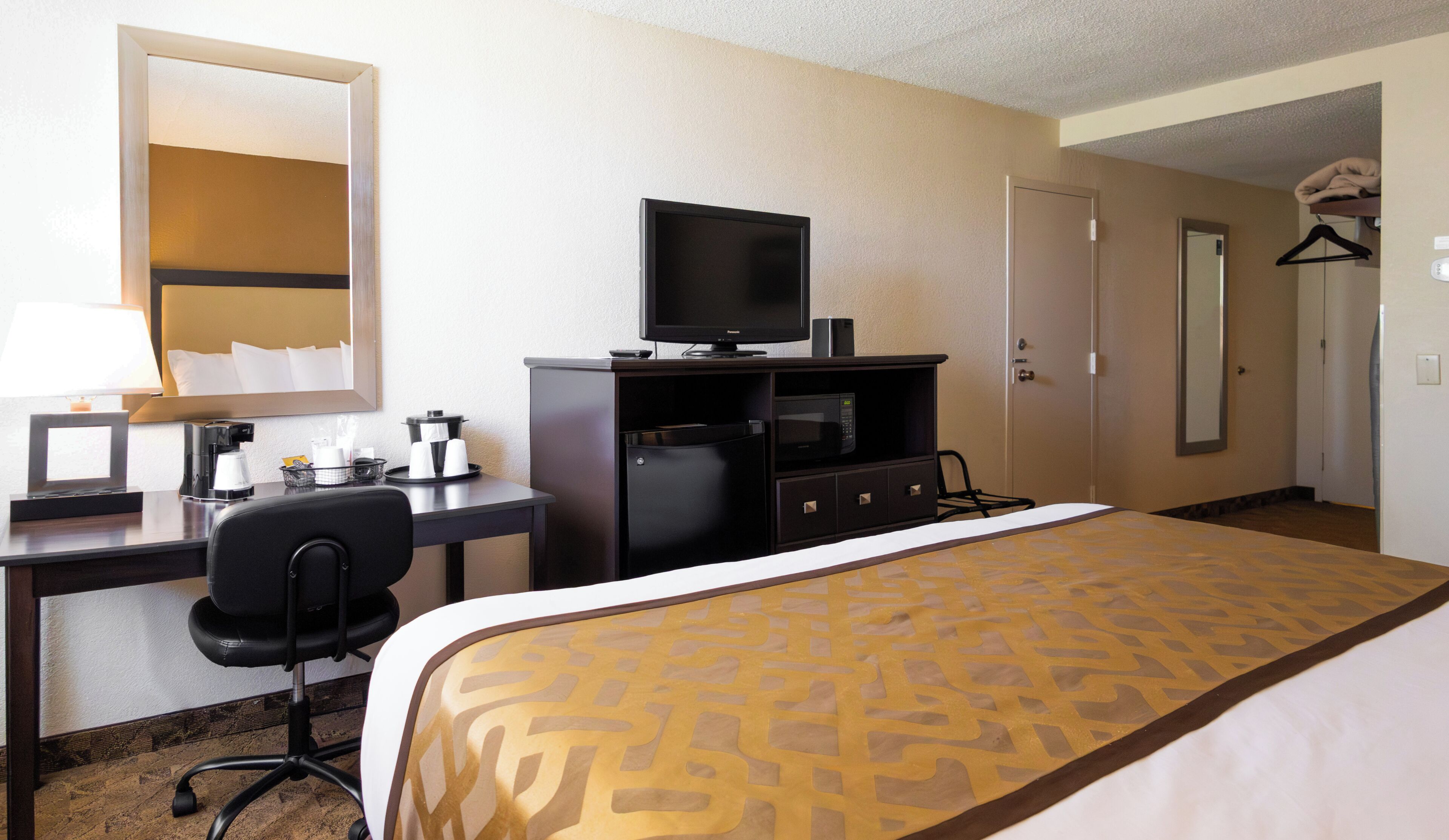 A hotel room with a bed, a desk with a computer, a television, a microwave, and a coffee maker.