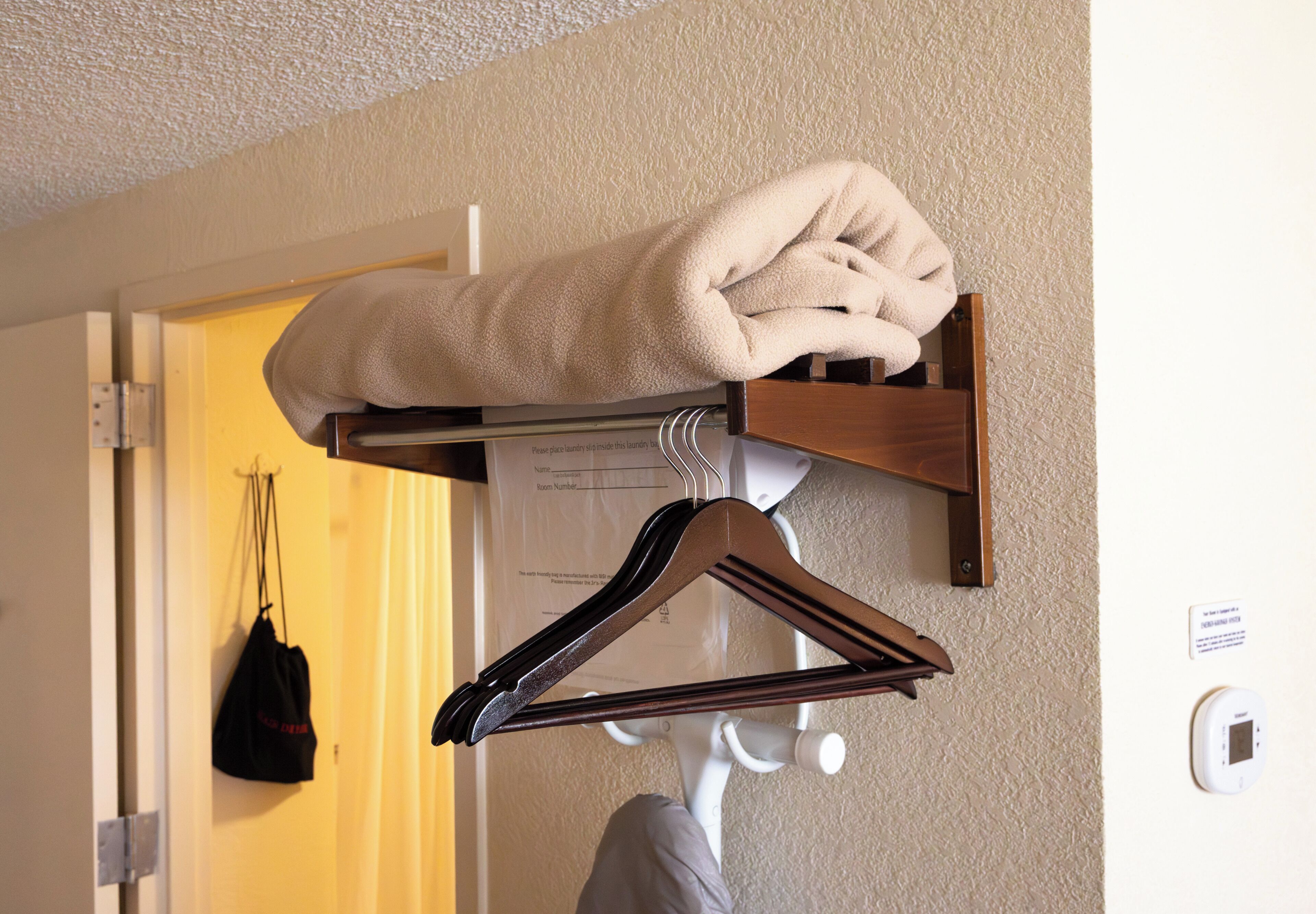 A towel rack with a folded towel and a hanger, a door with a bag hanging on it, and a thermostat on the wall.