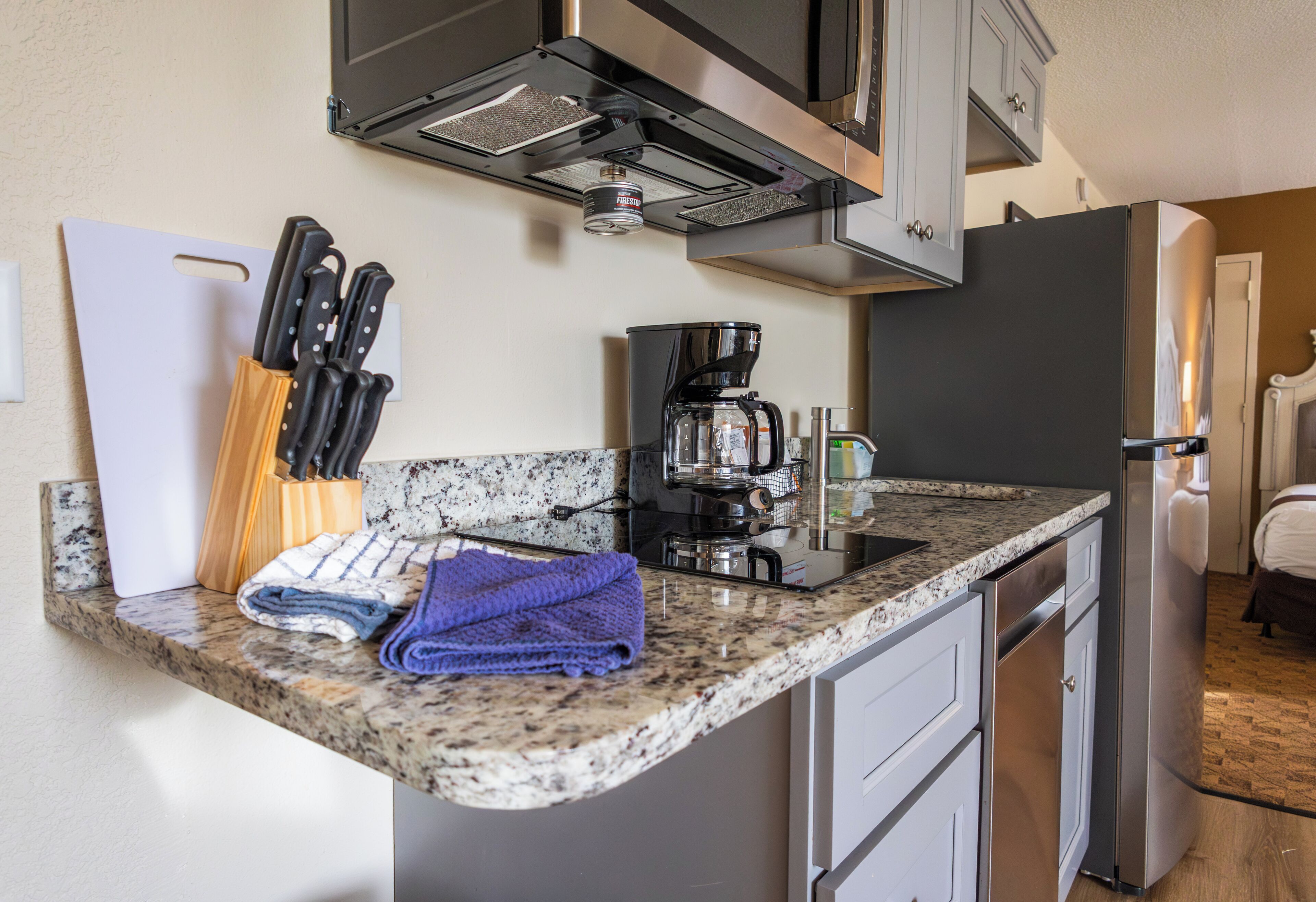 A kitchen with granite countertops, a coffee maker, a knife block, and a refrigerator.