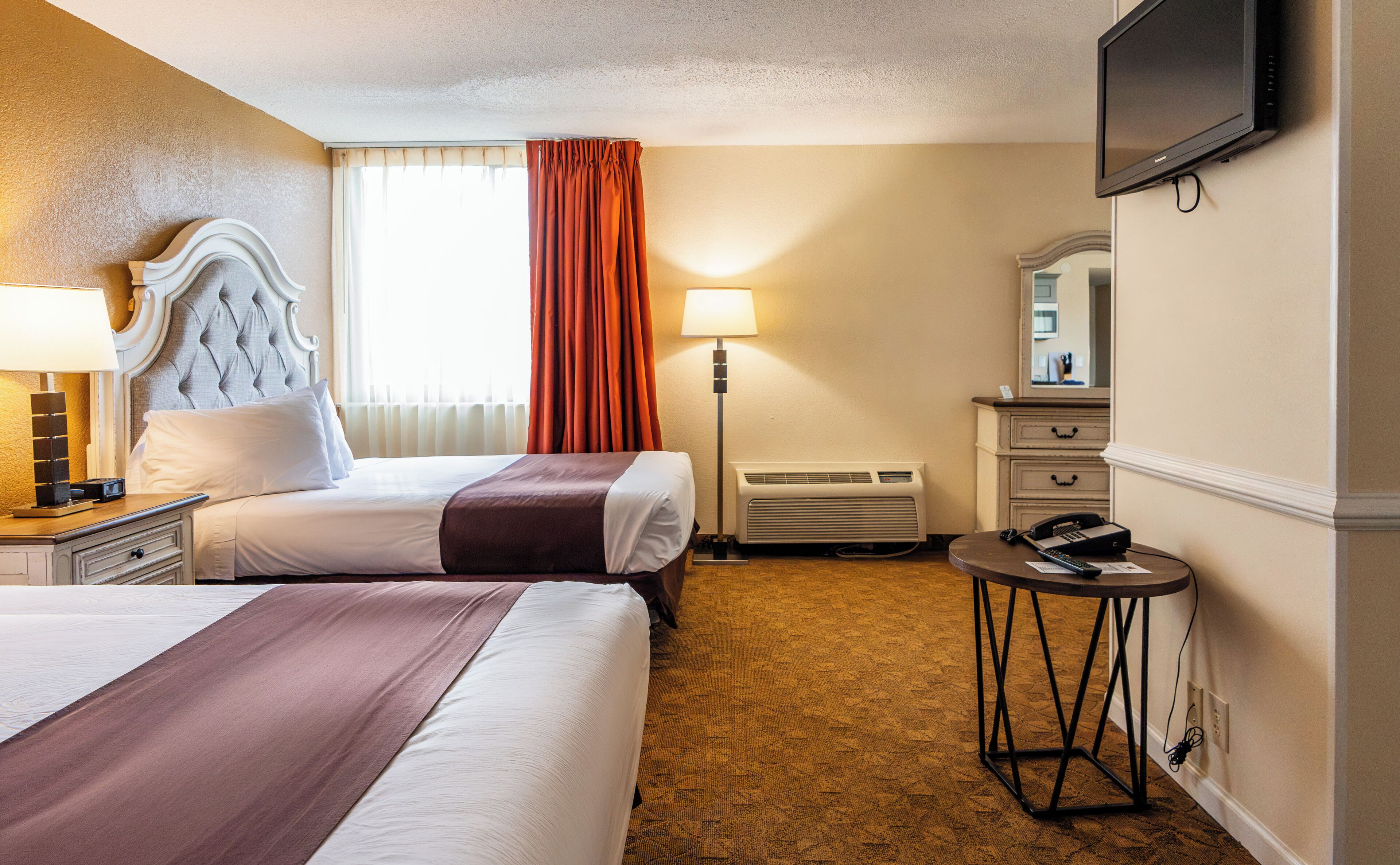 A hotel room with two beds, a flat-screen TV, a desk with a telephone, and a mirror.