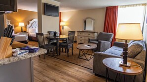 A hotel room with a bed, a dining table with chairs, a sofa, a TV, and a lamp. - Village Inn Clemmons/Winston Salem, Trademark by Wyndham (Clemmons)